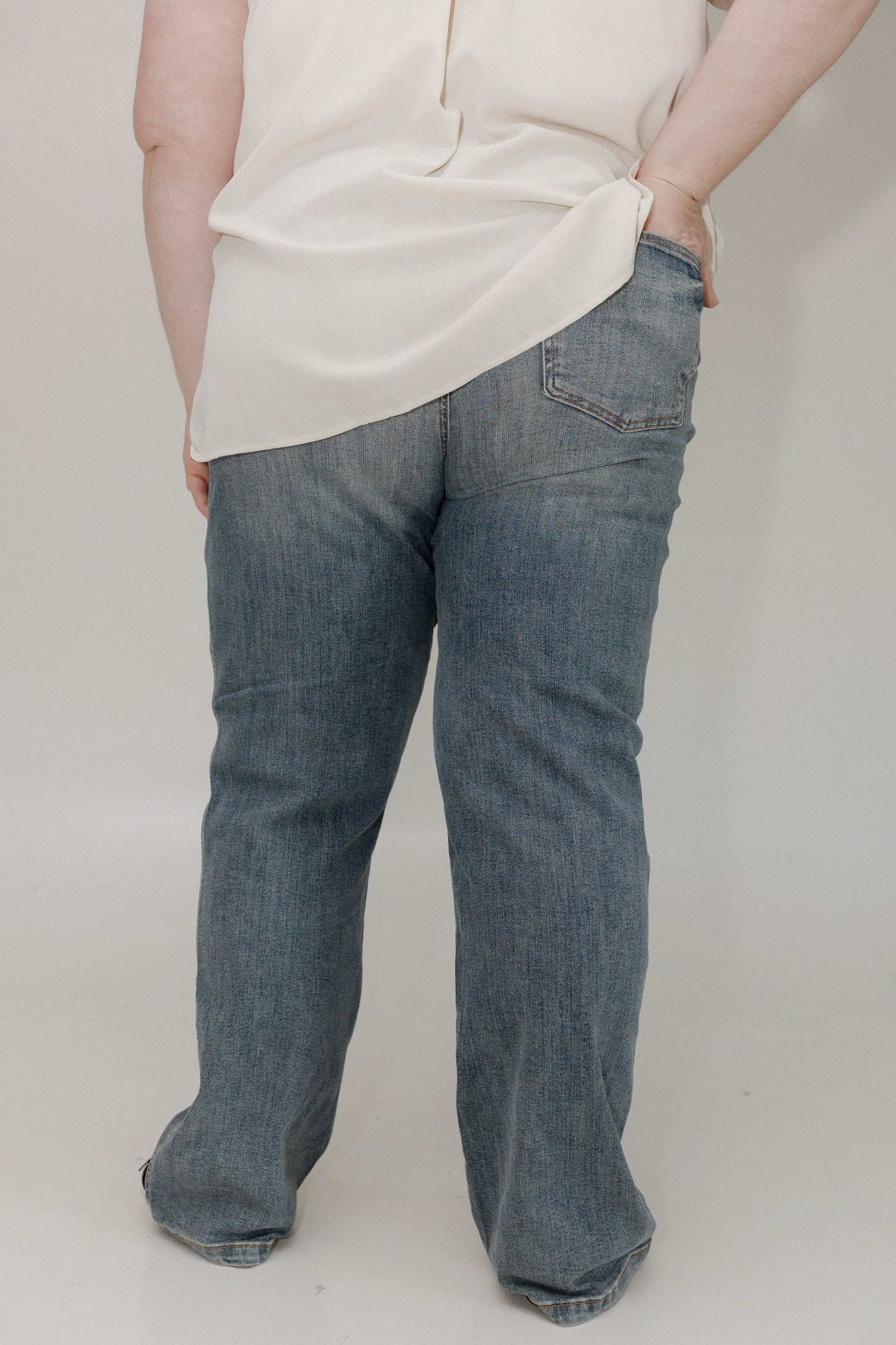Person wearing blue jeans and a white shirt on a plain background
