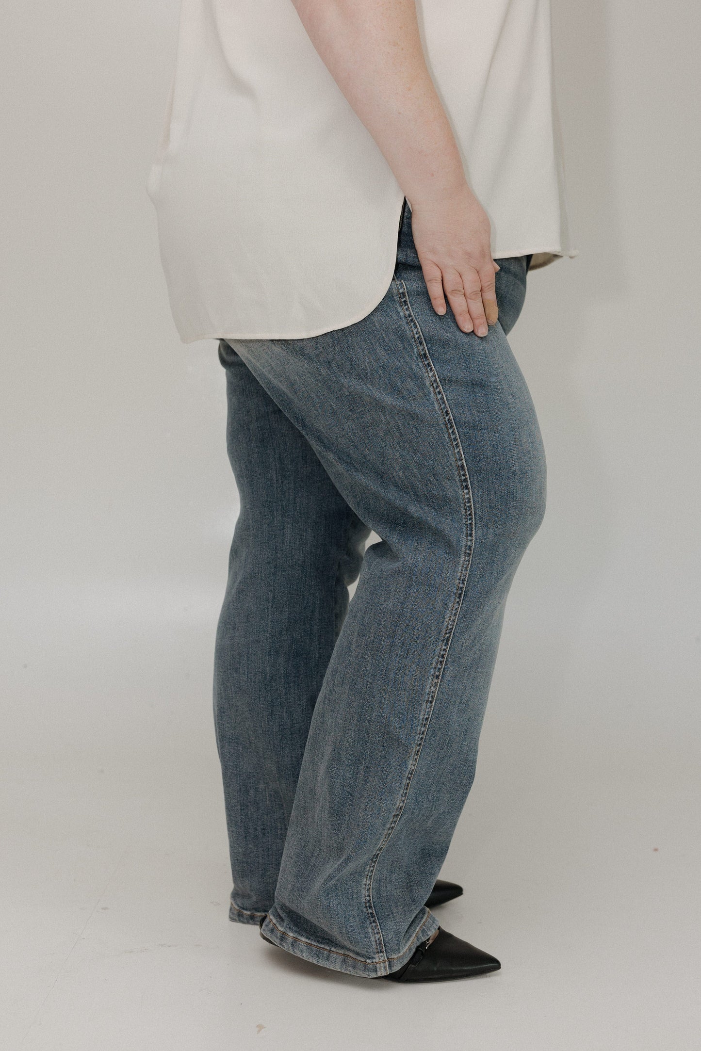 Person wearing a white shirt and blue jeans on a plain background
