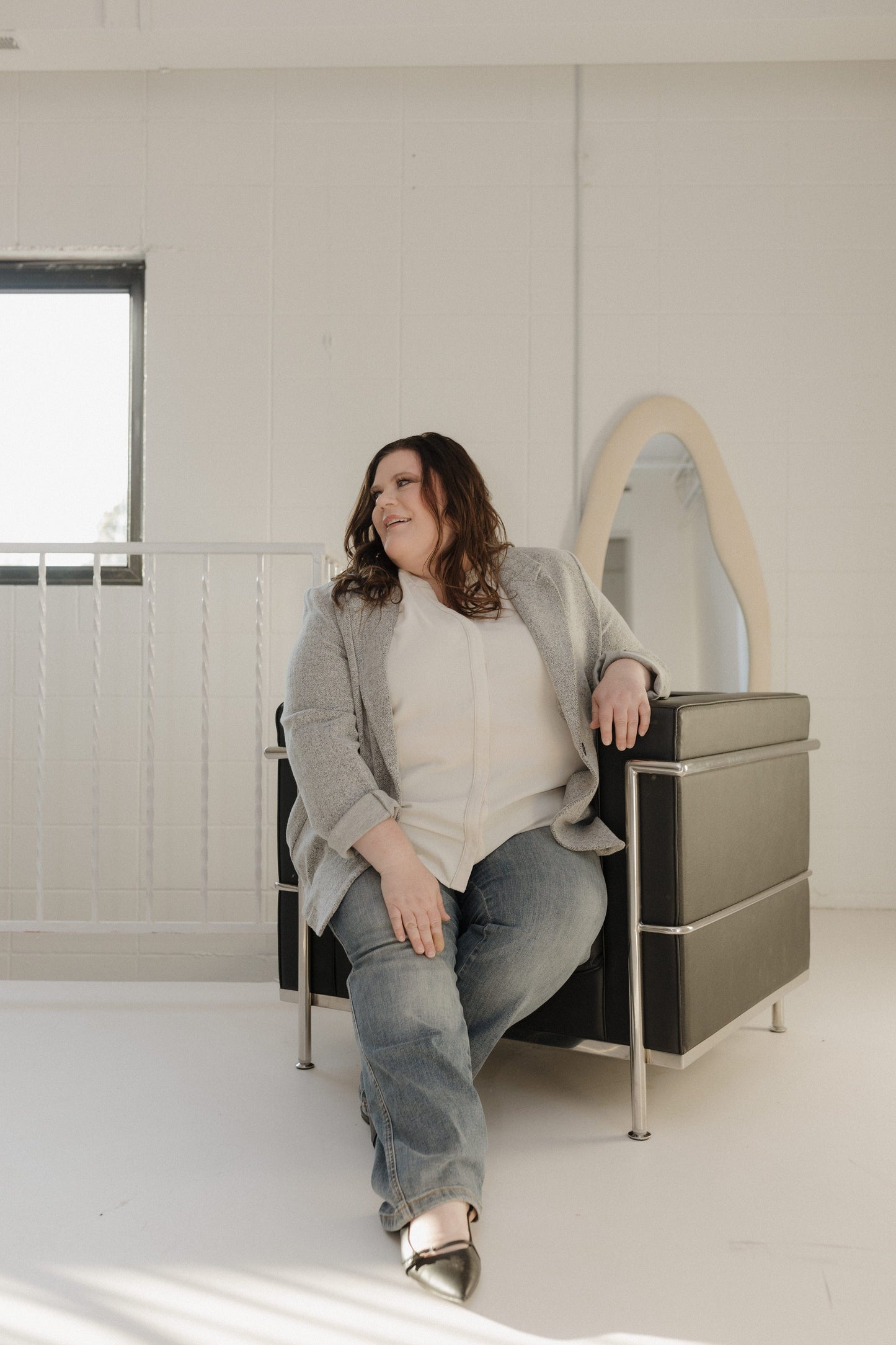 Woman sitting on a modern chair in a minimalistic room with a mirror.