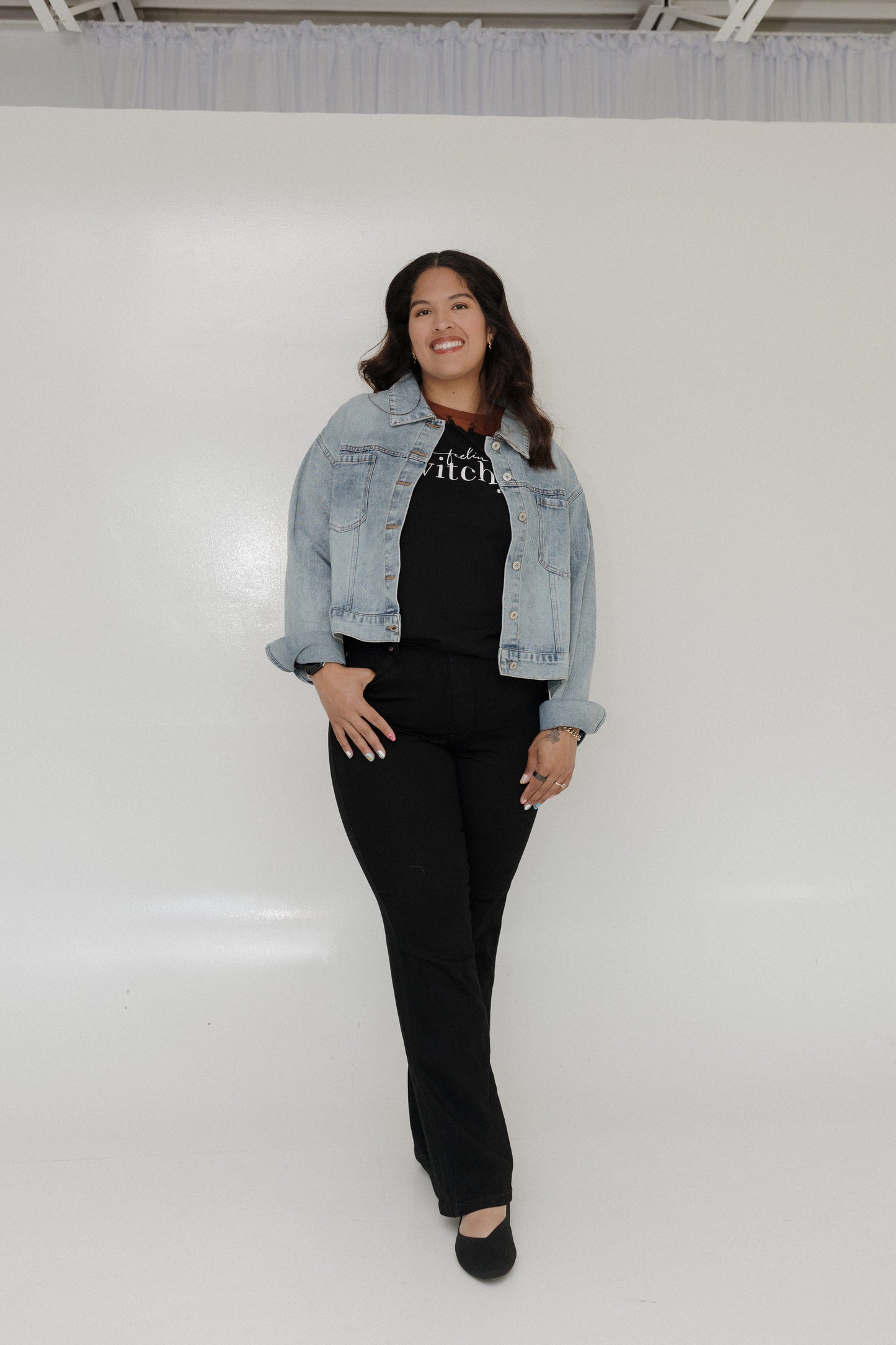 Woman wearing a denim jacket over a black outfit on a white background