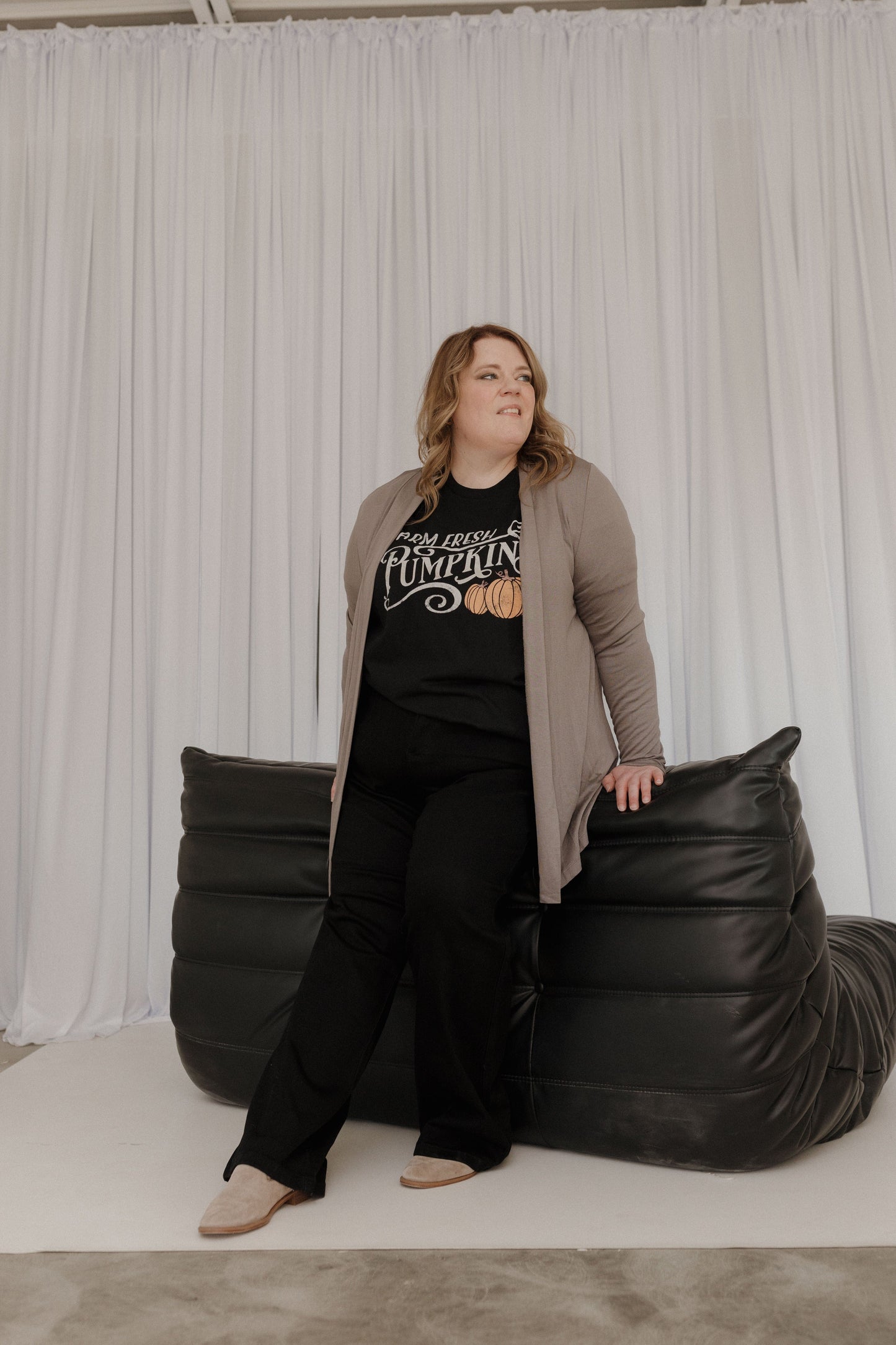 Woman posing with a large black bean bag chair against a white curtain.