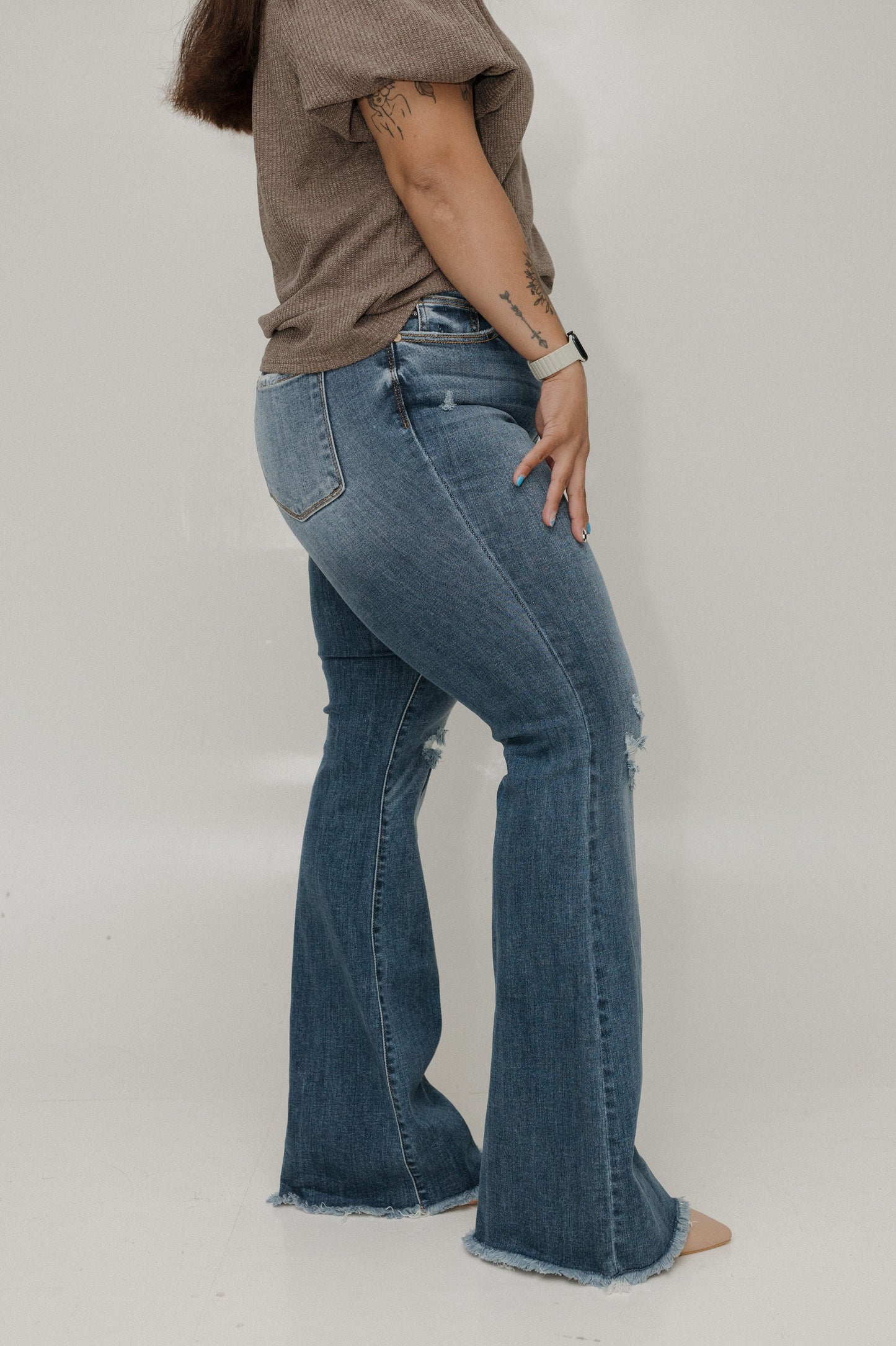 Person wearing blue jeans and a brown shirt on a plain background