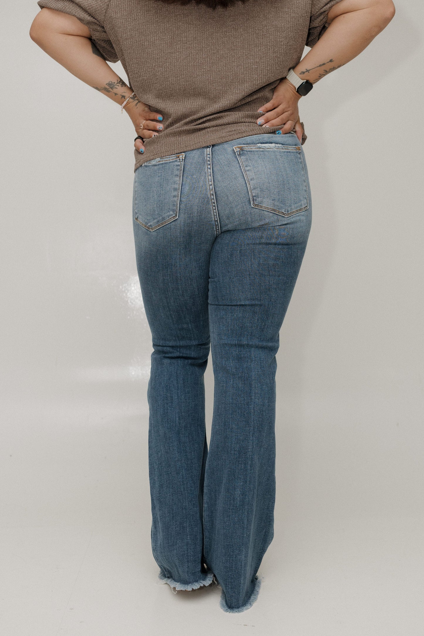 Person wearing blue jeans and a brown shirt on a plain background