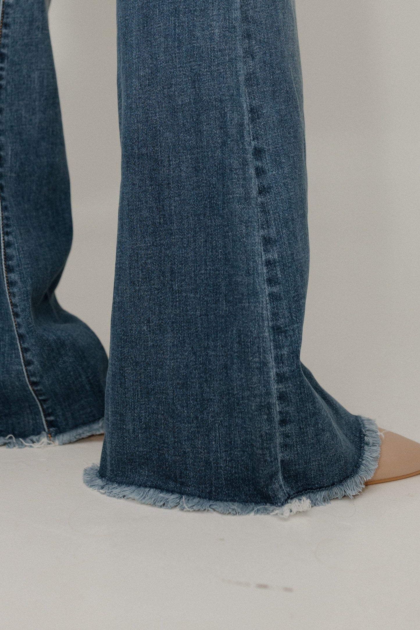 Close-up of blue jeans with frayed hem on a neutral background