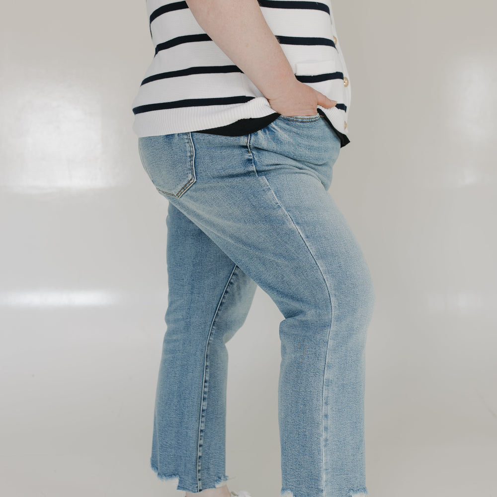 Person wearing a black and white striped shirt, blue jeans, and white sneakers on a plain background