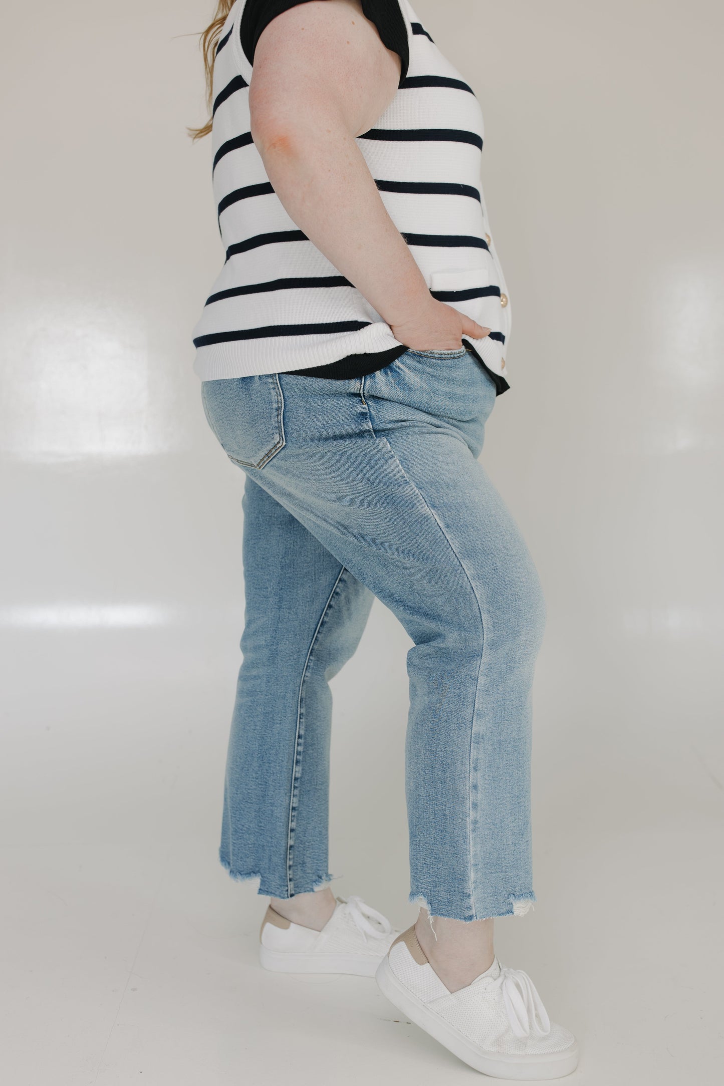 Person wearing a black and white striped shirt, blue jeans, and white sneakers on a plain background