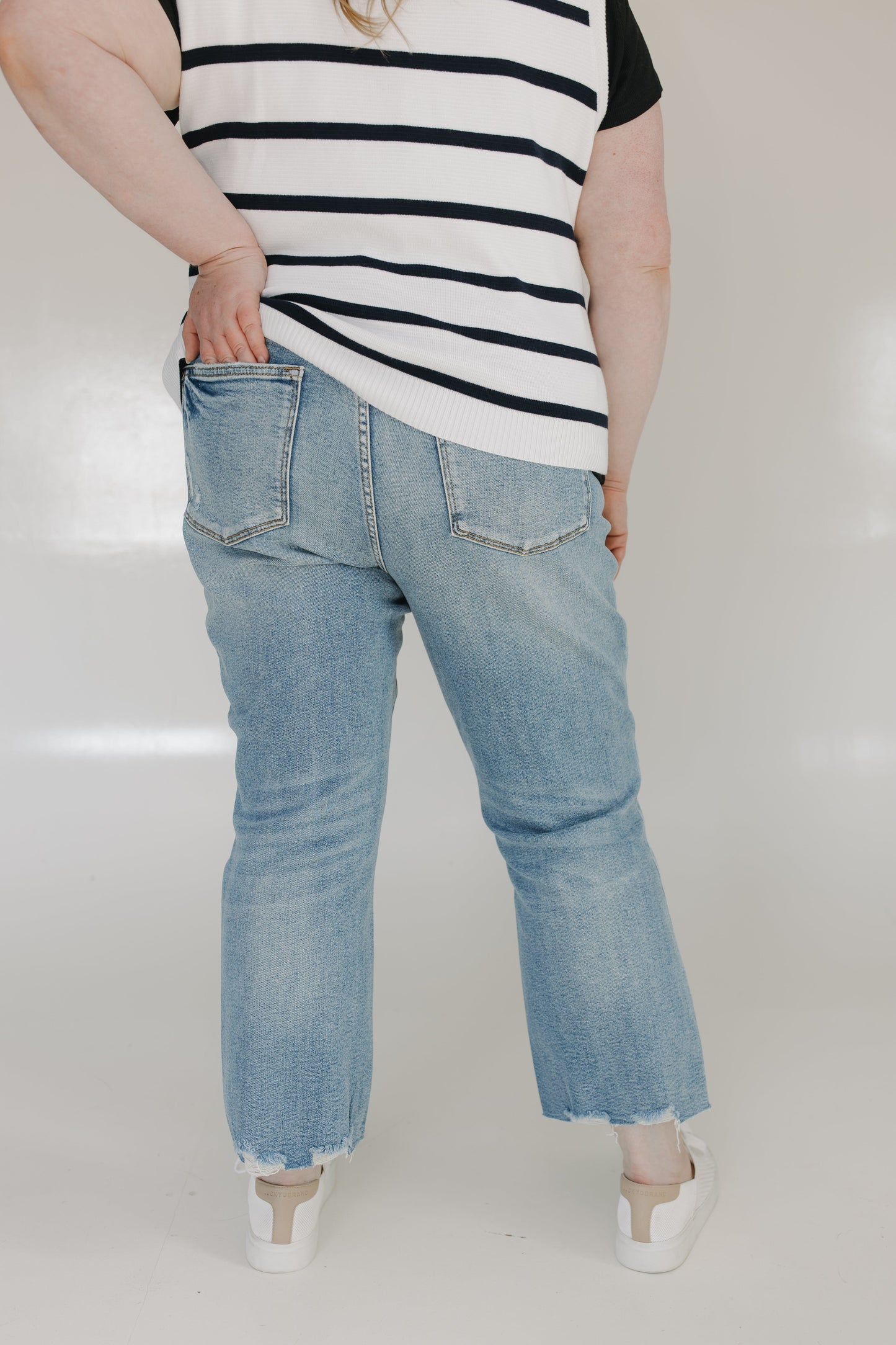 Person wearing a striped shirt and light blue jeans on a white background