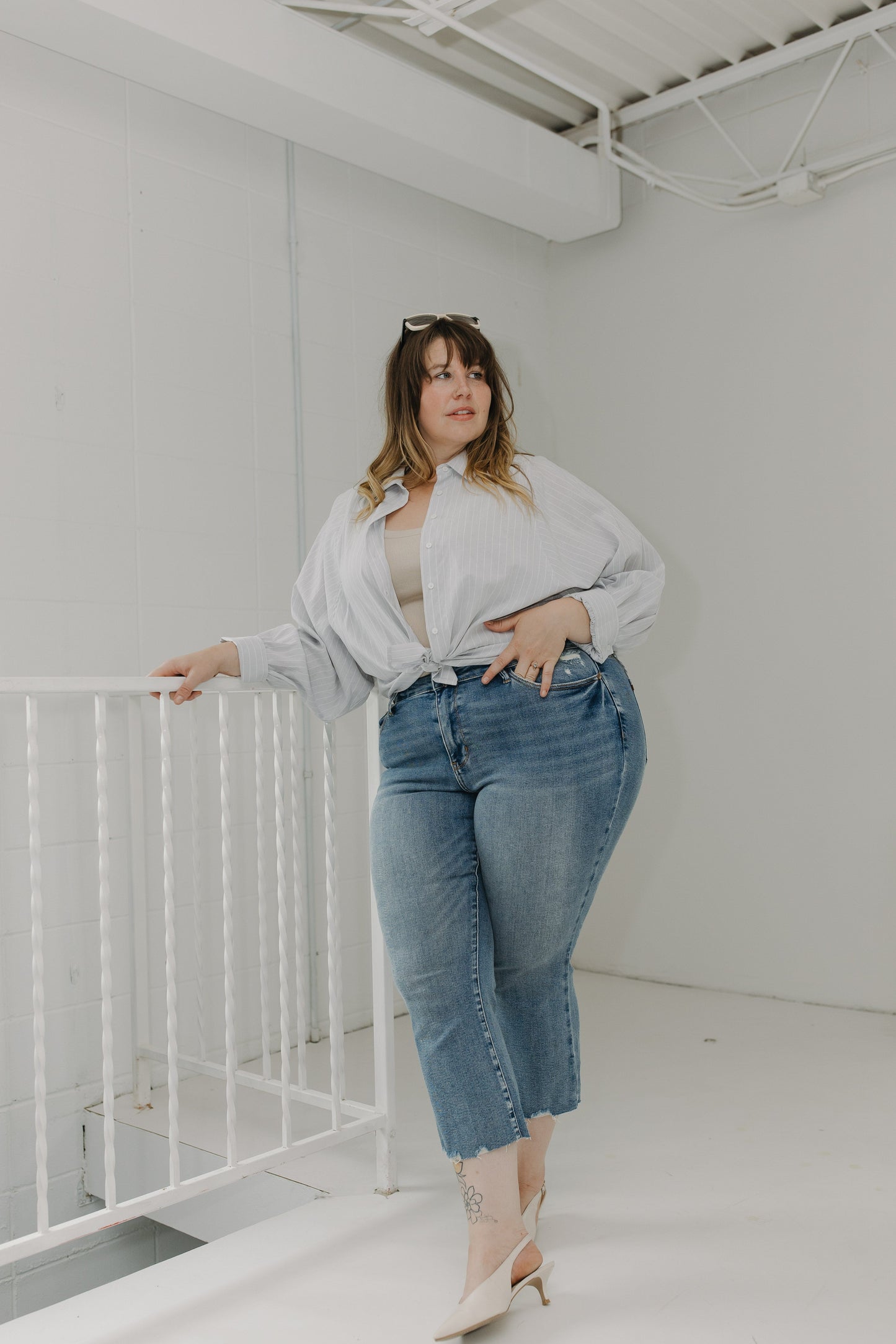 Woman in a white shirt and blue jeans standing in a minimalistic room.