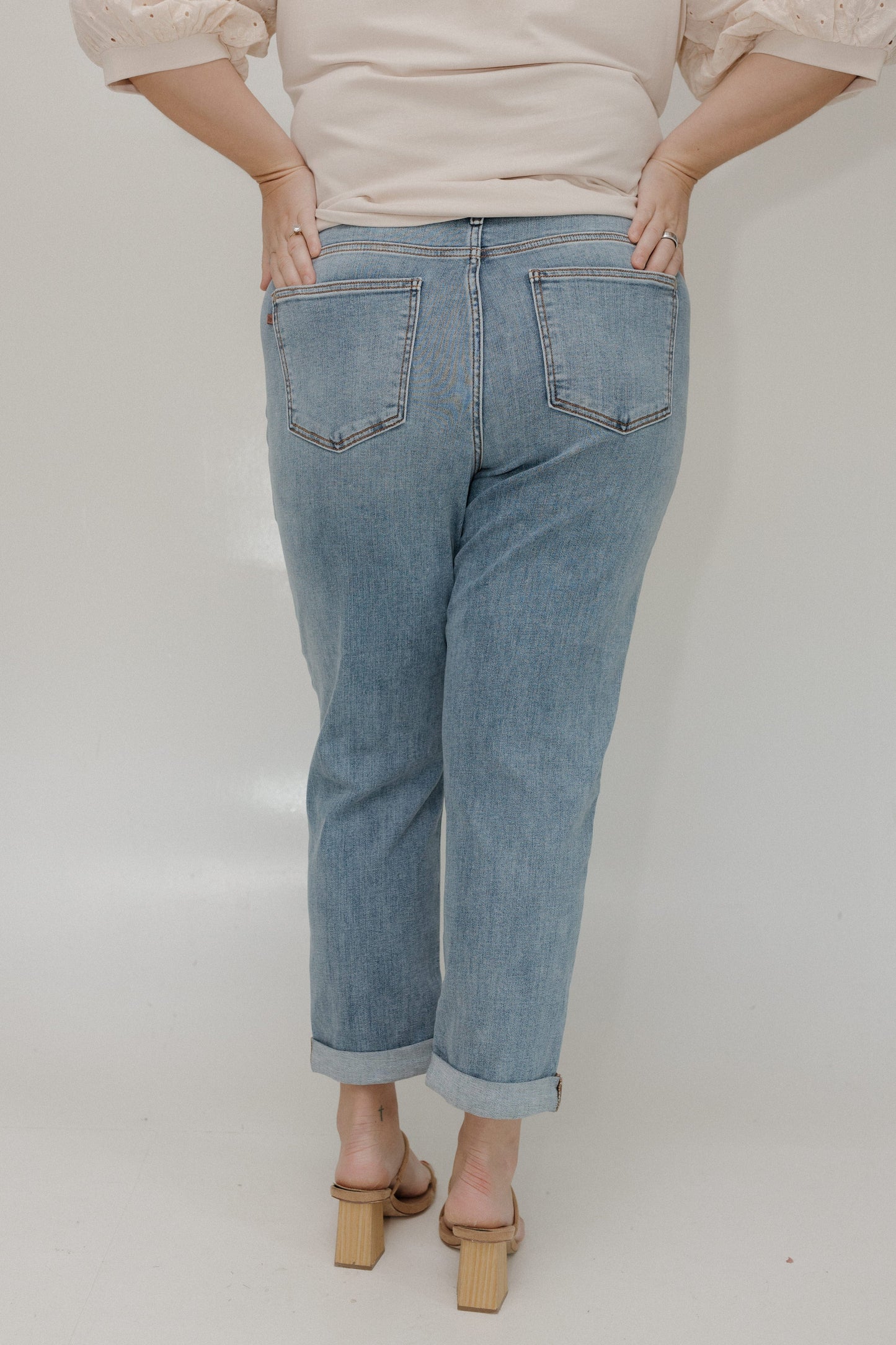 Person wearing light blue jeans and a beige top on a plain background