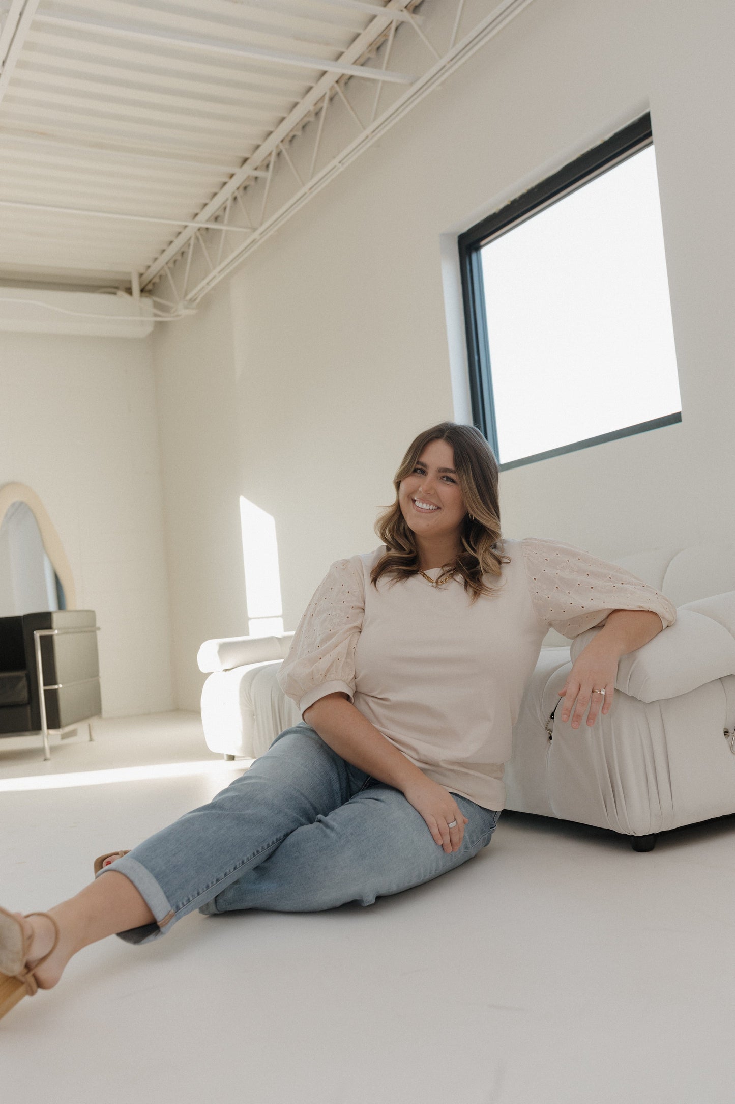 Woman sitting on a white couch in a bright, minimalistic room.