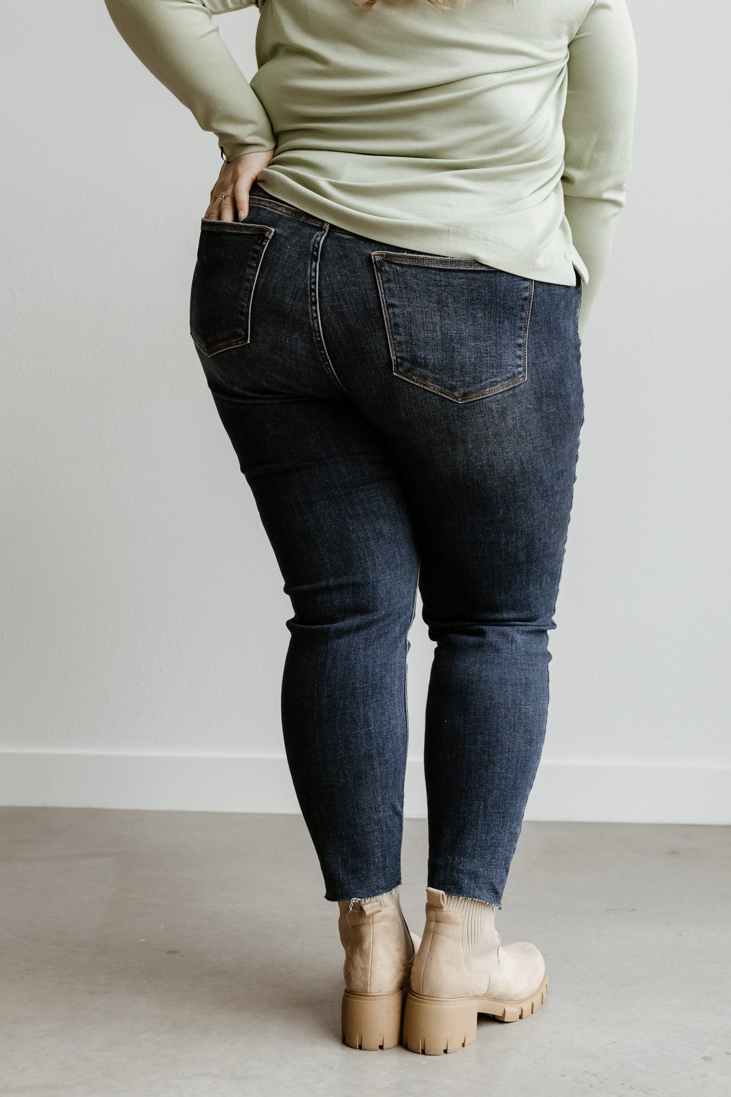 A person is seen from the back wearing a light green top, tan ankle boots, and Judy Blue mid-rise skinny jeans, creating a stylish and cohesive look.