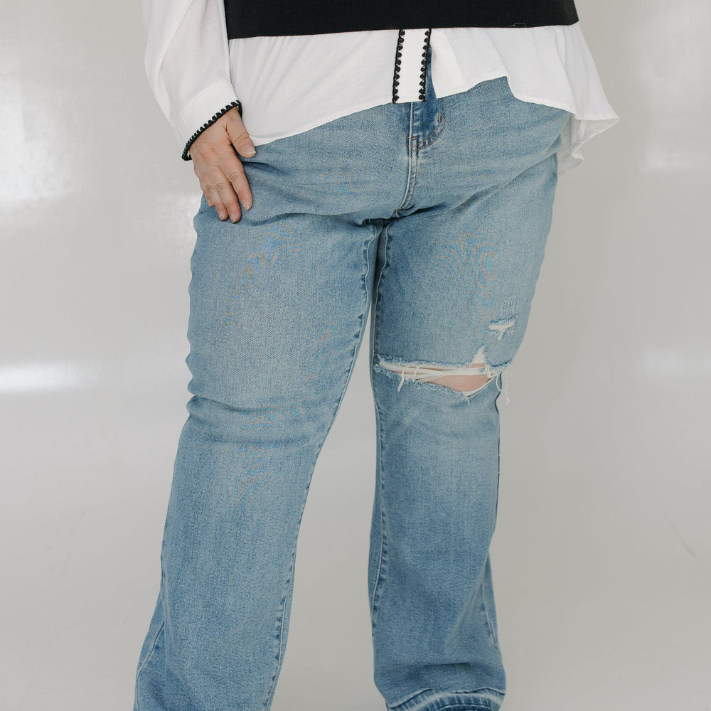 Person wearing a white shirt, black vest, and blue jeans with a white background