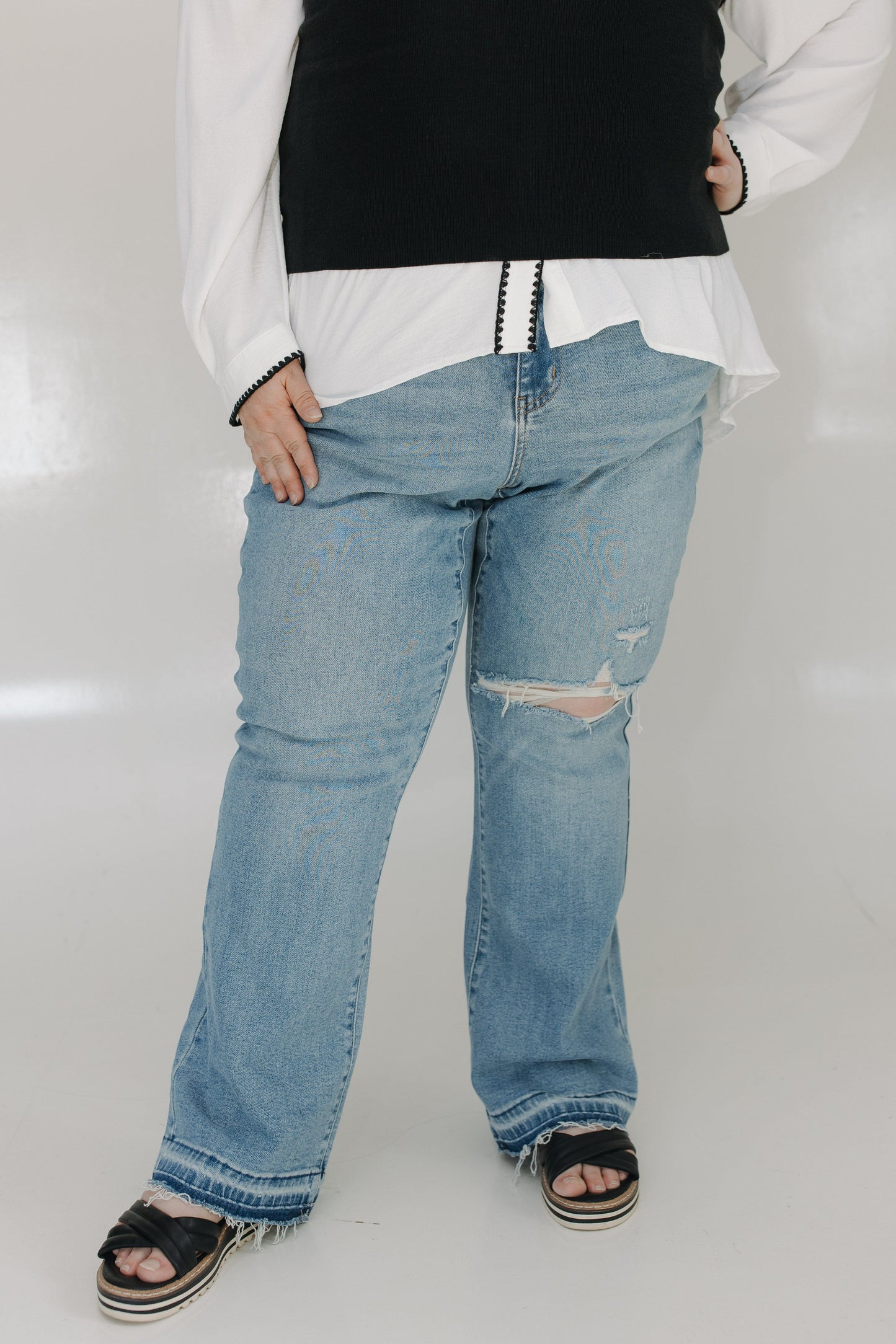 Person wearing a white shirt, black vest, and blue jeans with a white background