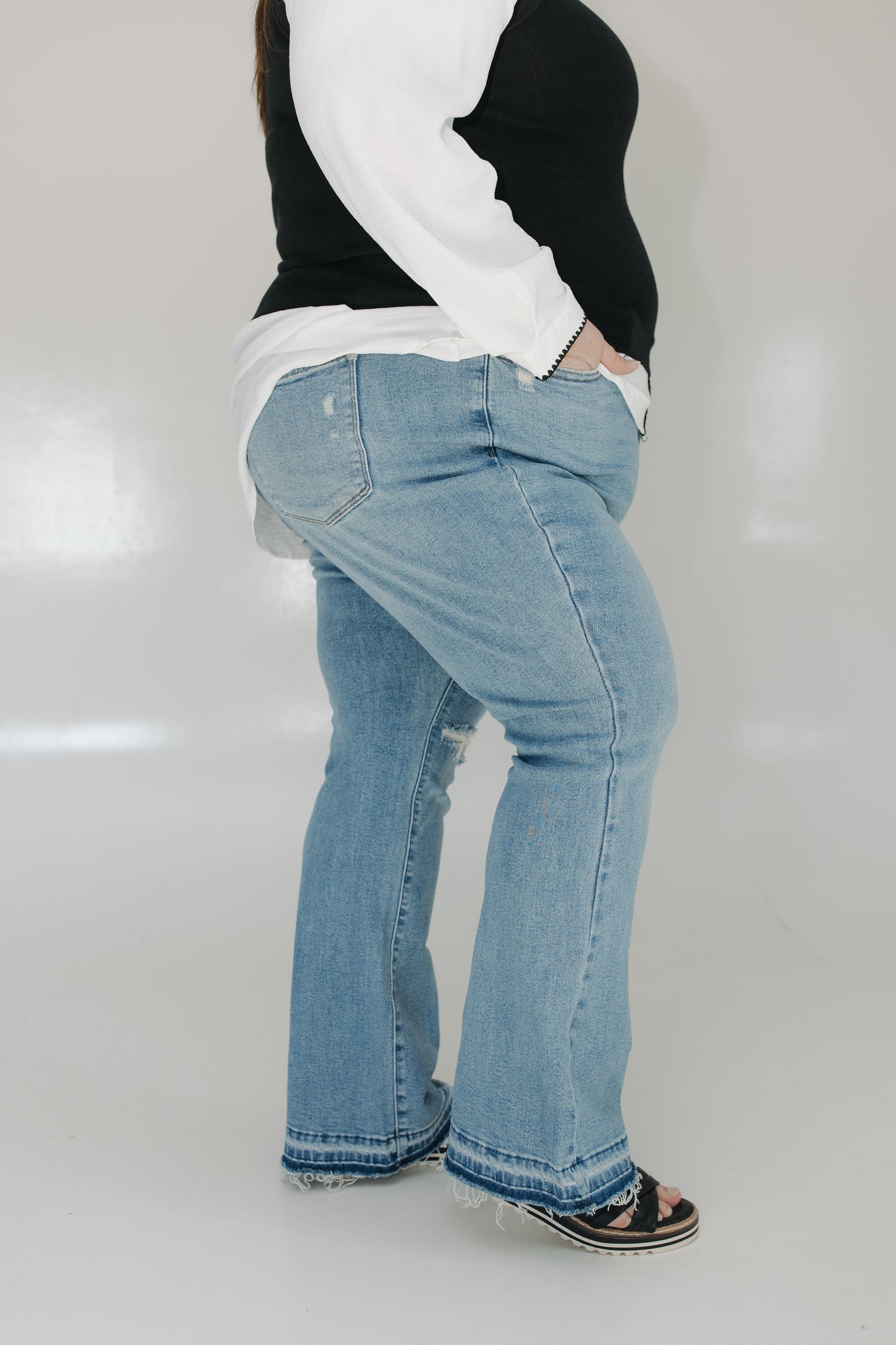 Person wearing light blue jeans and a black and white top on a plain background