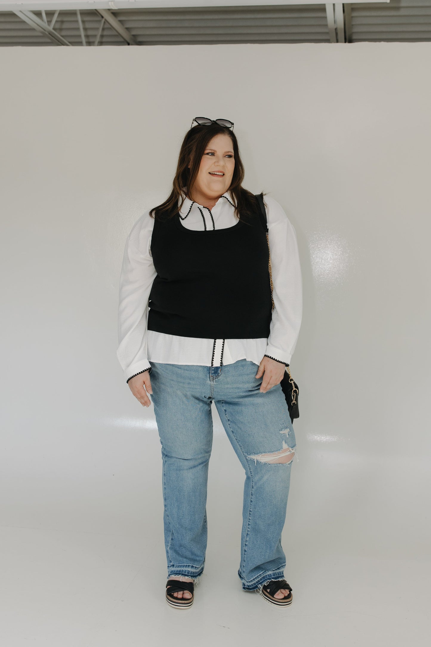 Person wearing a black vest, white shirt, and blue jeans against a plain background