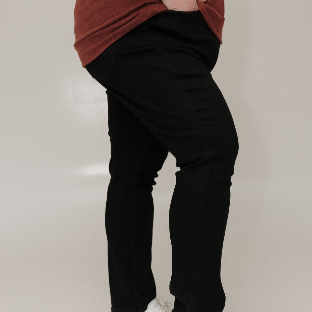 Person wearing a brown sweater, black pants, and white shoes on a plain background