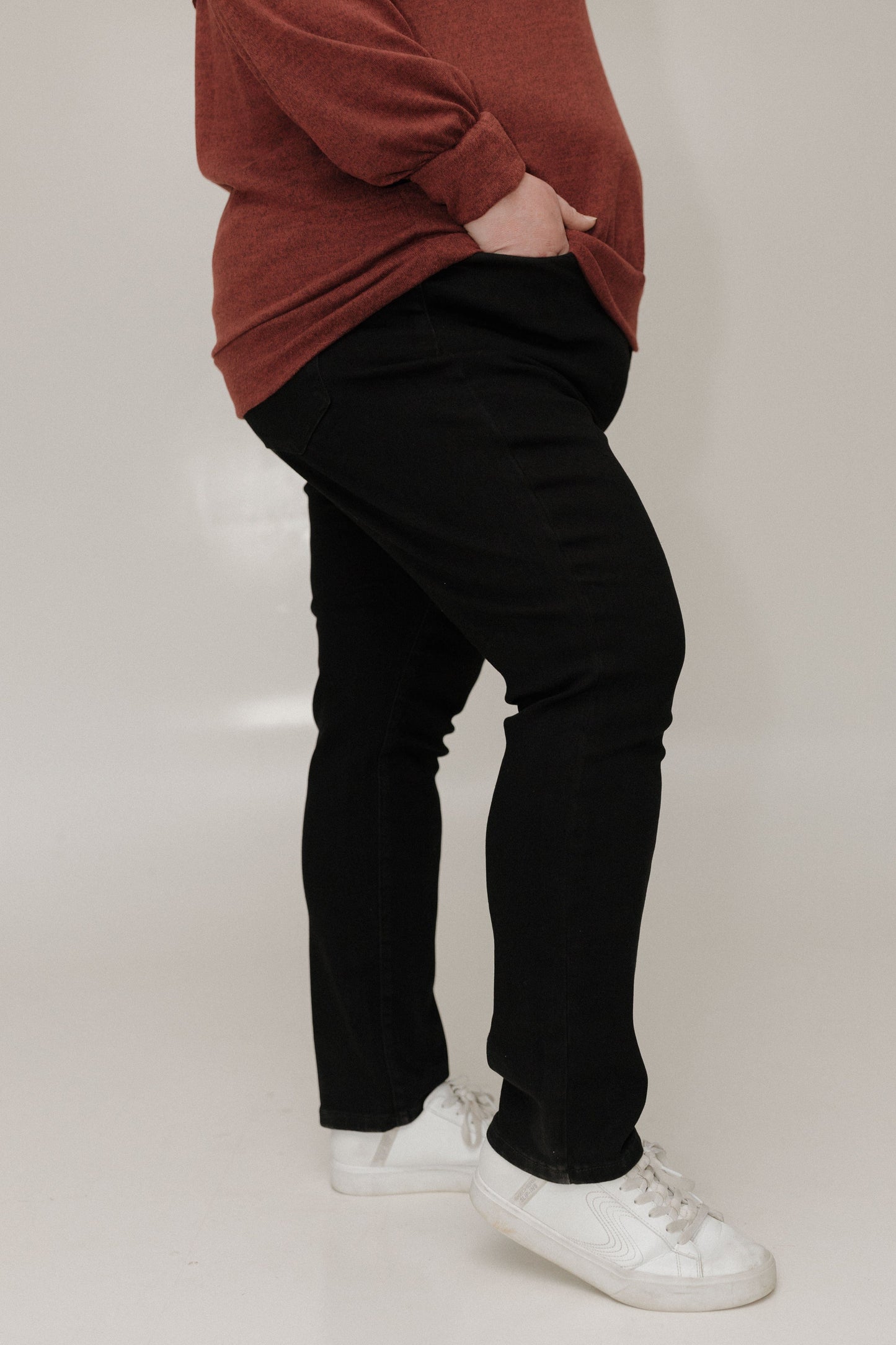 Person wearing a brown sweater, black pants, and white shoes on a plain background