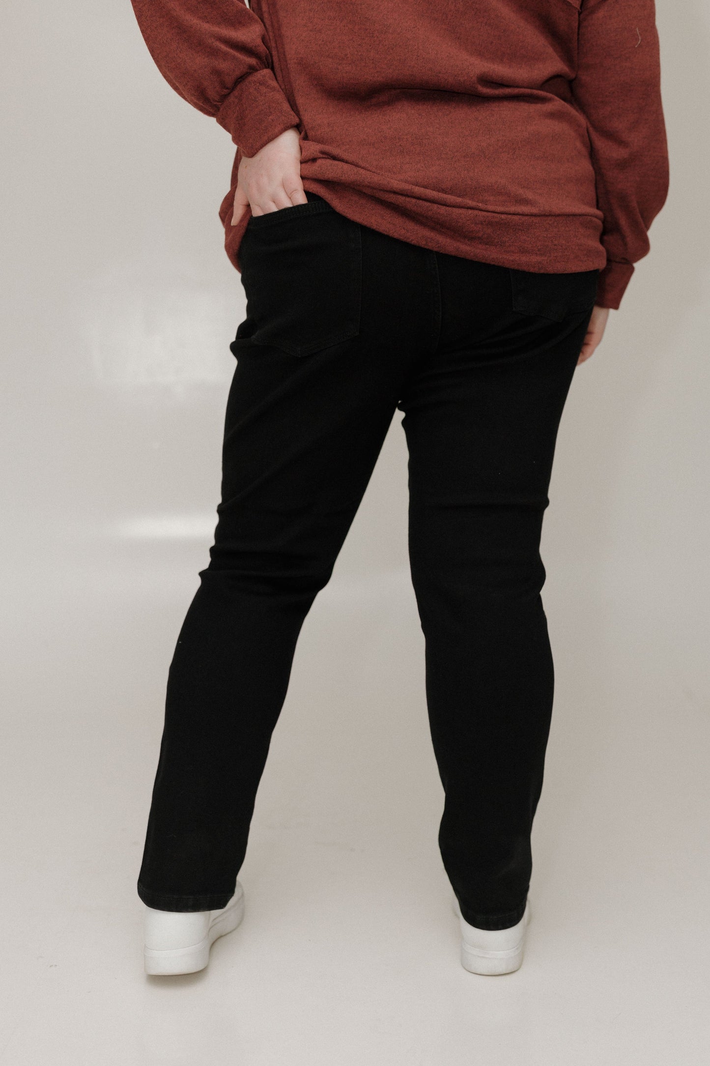 Person wearing a brown sweatshirt and black pants on a white background
