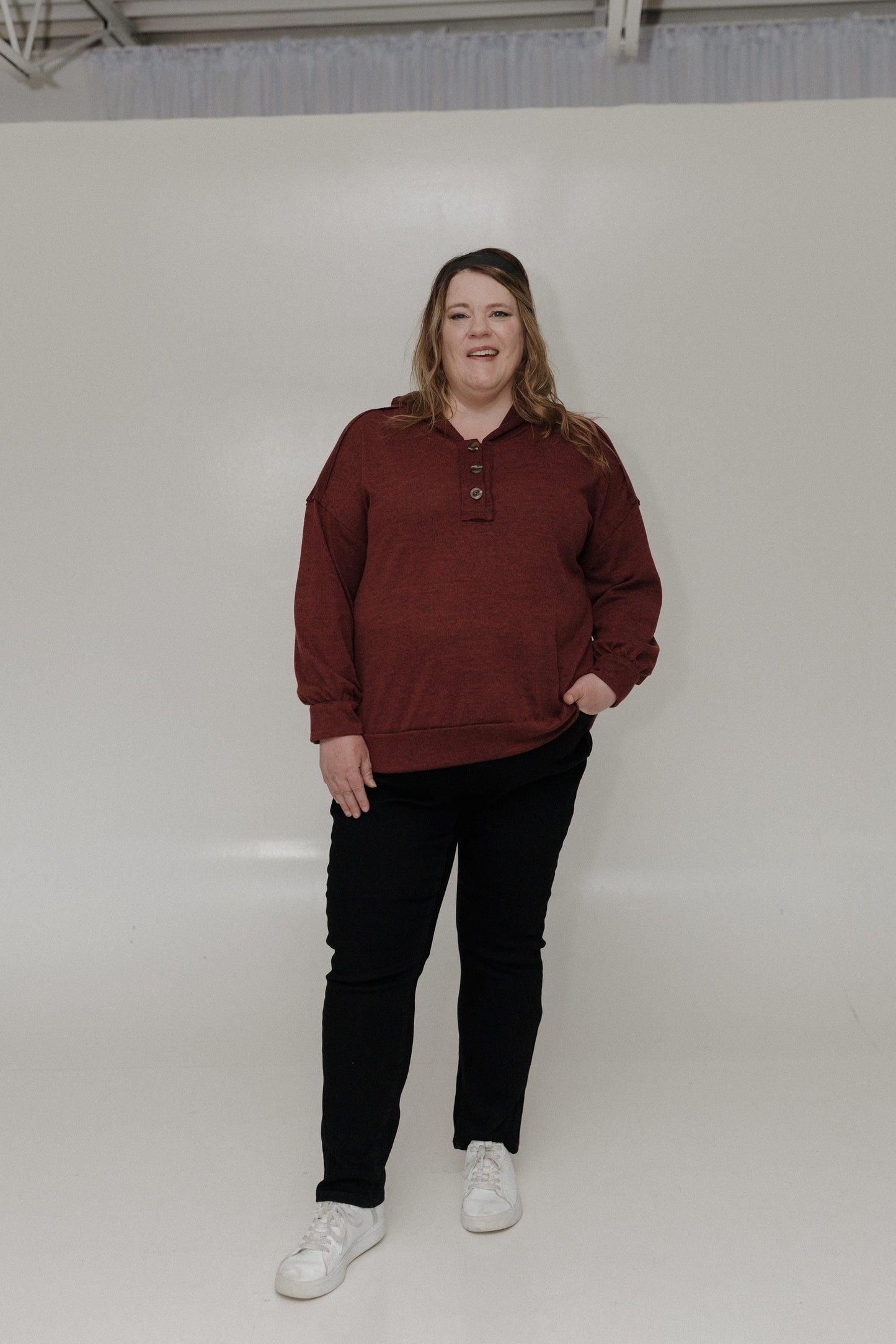 Person wearing a maroon hoodie and black pants standing against a white background
