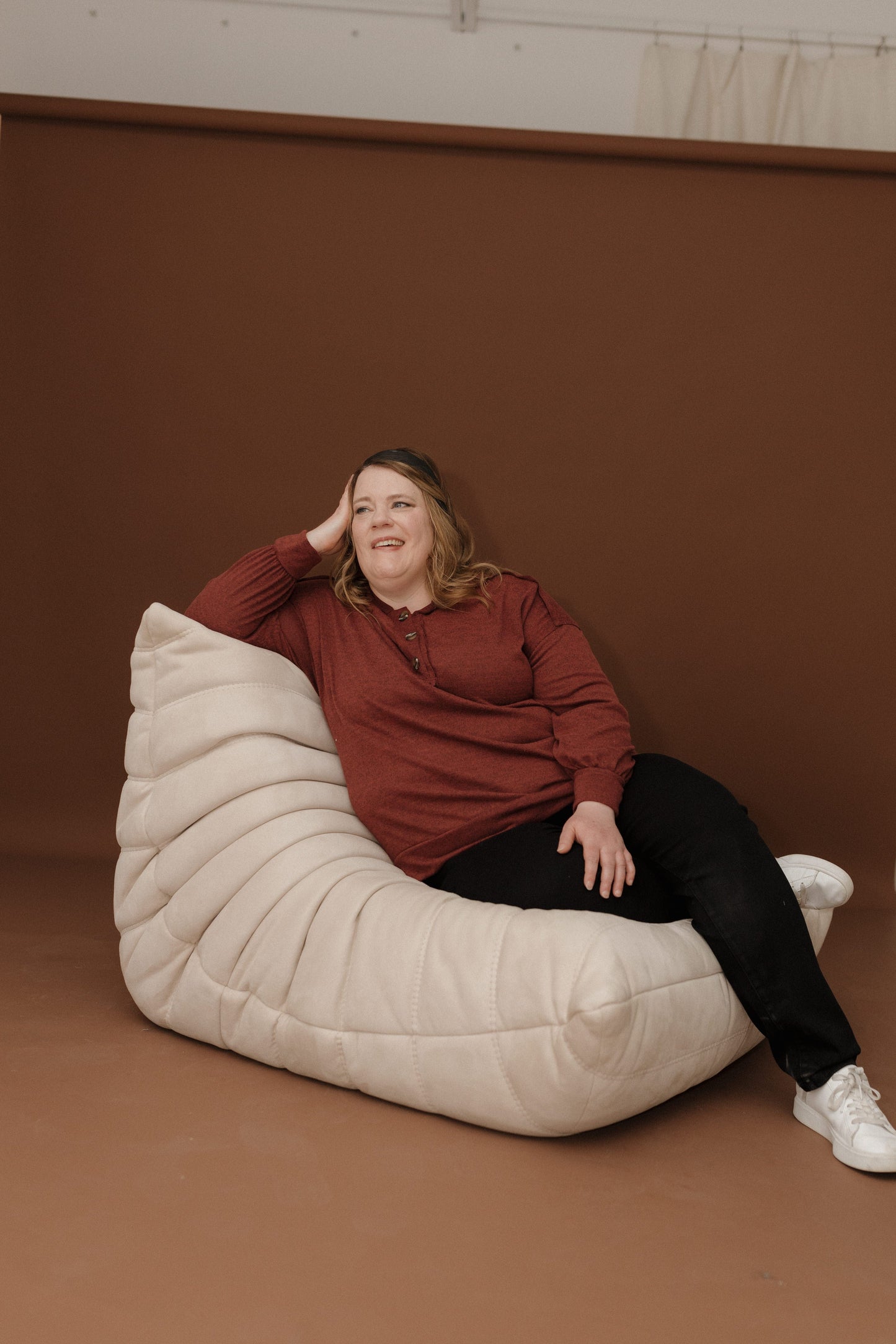 Woman sitting on a large white bean bag chair against a brown wall.
