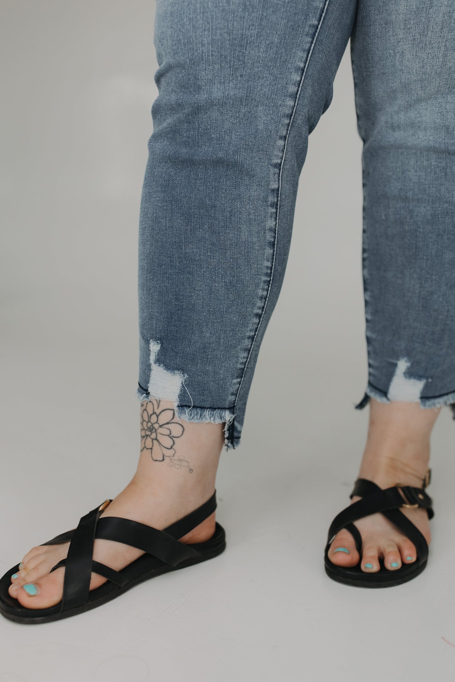 Person wearing black sandals and ripped blue jeans on a plain background