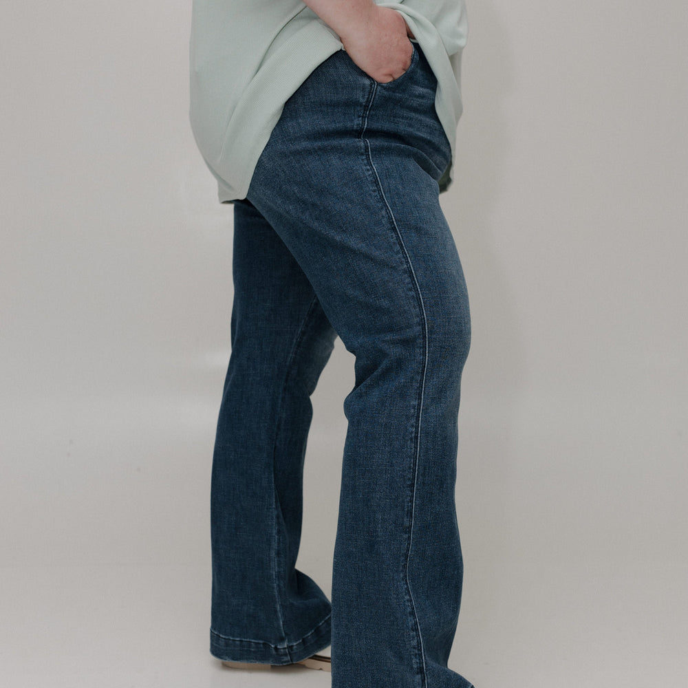 Person wearing a light green shirt and blue jeans on a plain background