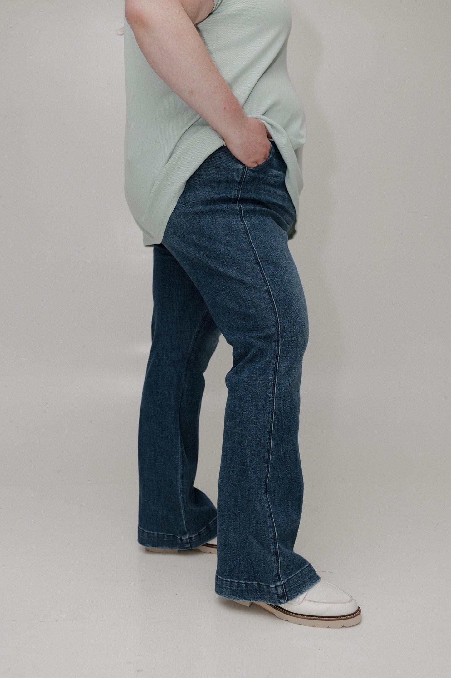 Person wearing a light green shirt and blue jeans on a plain background