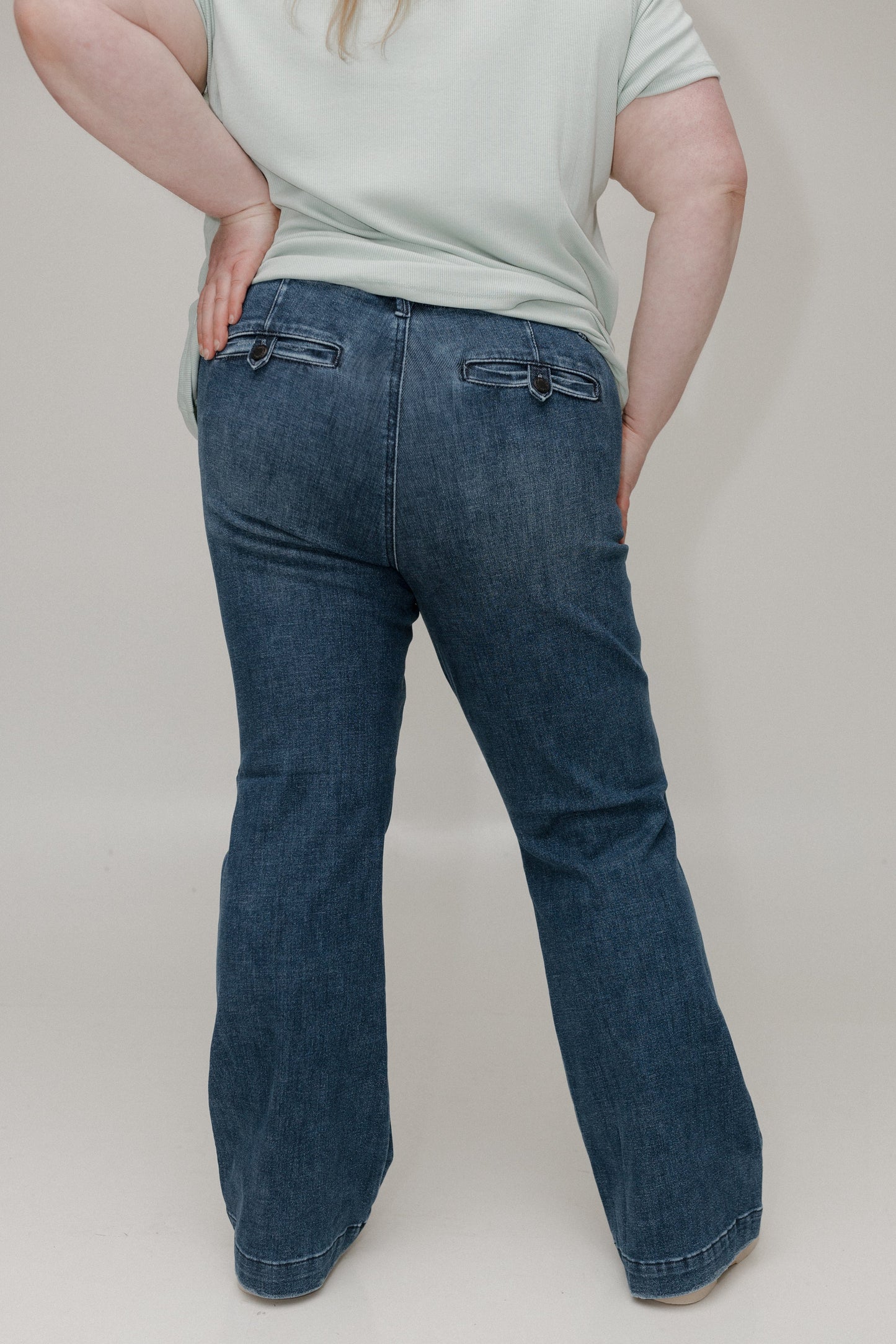 Person wearing blue jeans and a light-colored shirt on a plain background