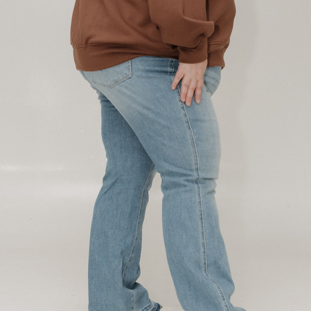 Person wearing a brown sweatshirt and blue jeans on a plain background