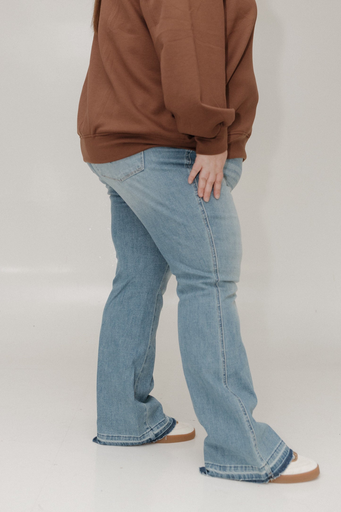 Person wearing a brown sweatshirt and blue jeans on a plain background