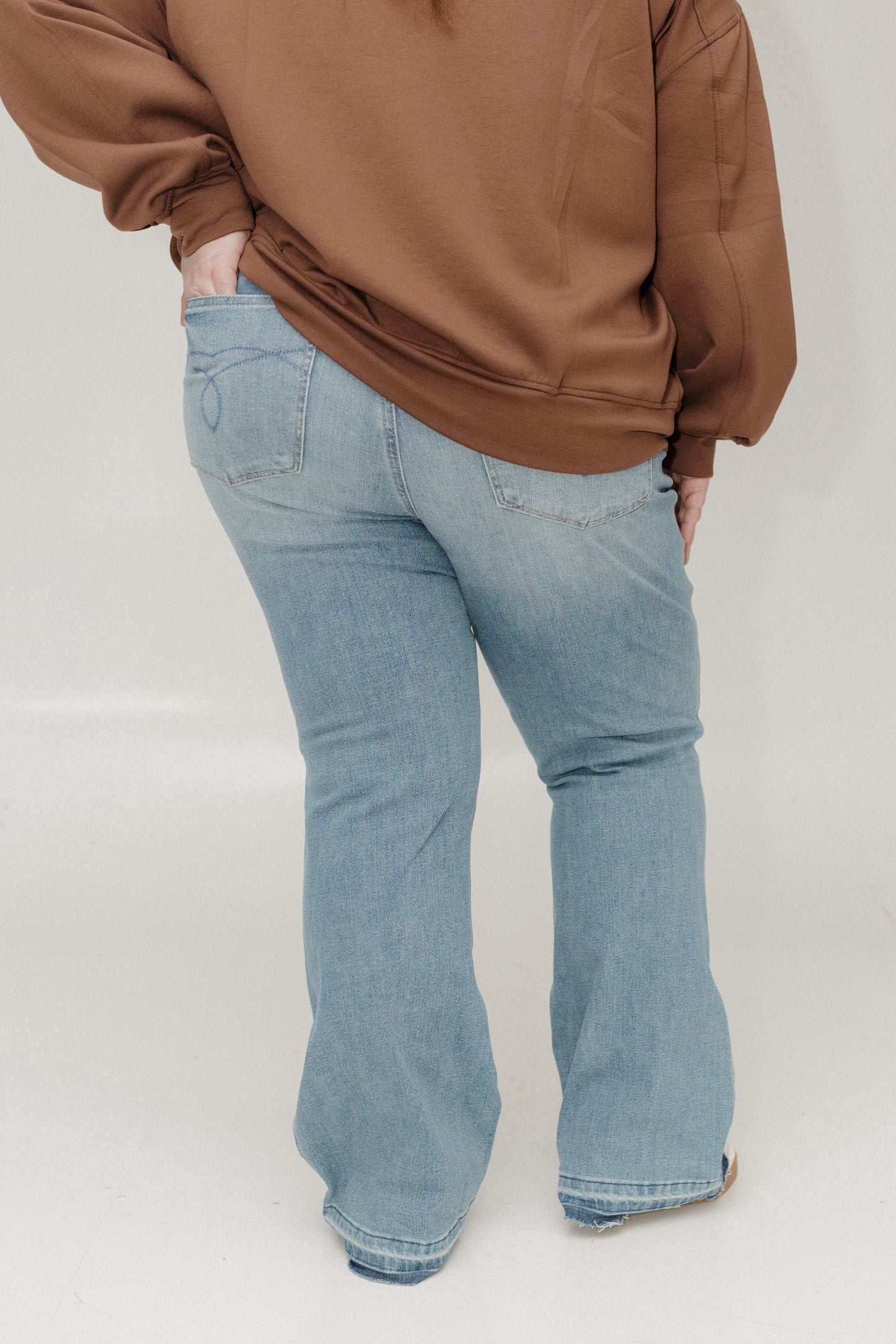 Person wearing a brown sweatshirt and light blue jeans on a white background