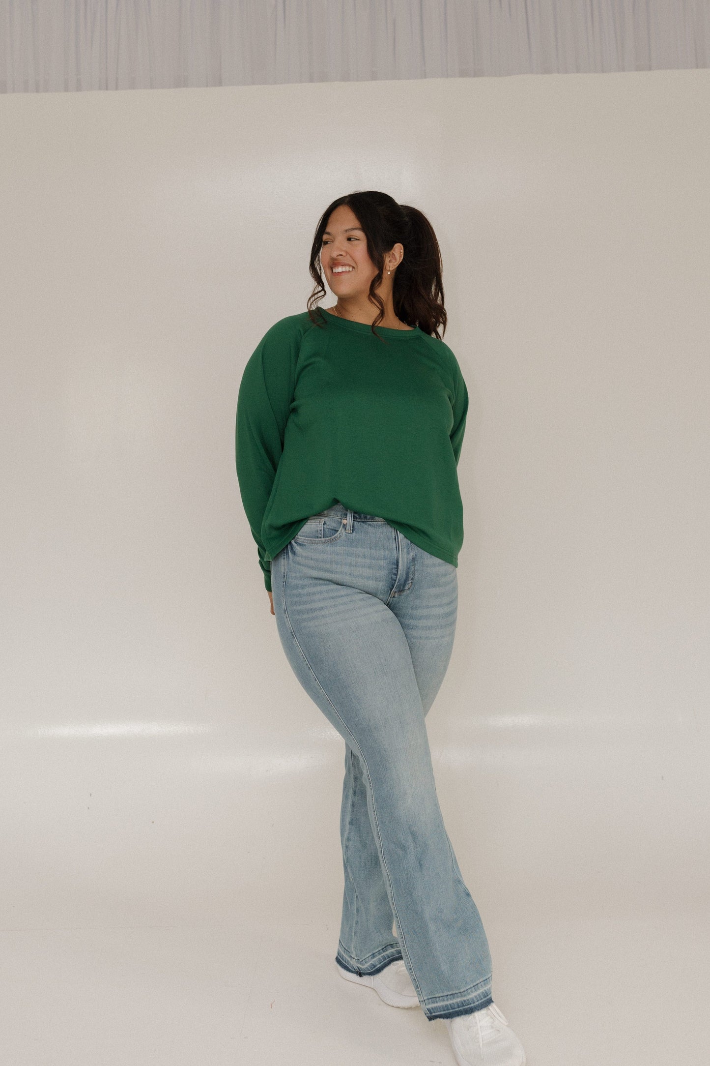 Woman wearing a green sweater and light blue jeans on a white background