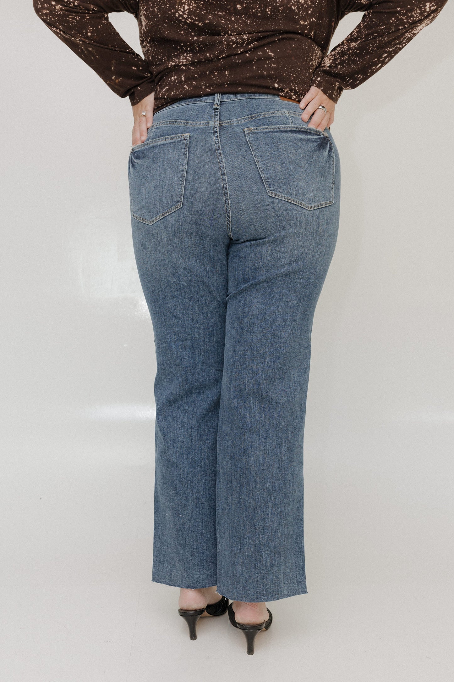 Person wearing blue jeans and a brown sequin top on a white background