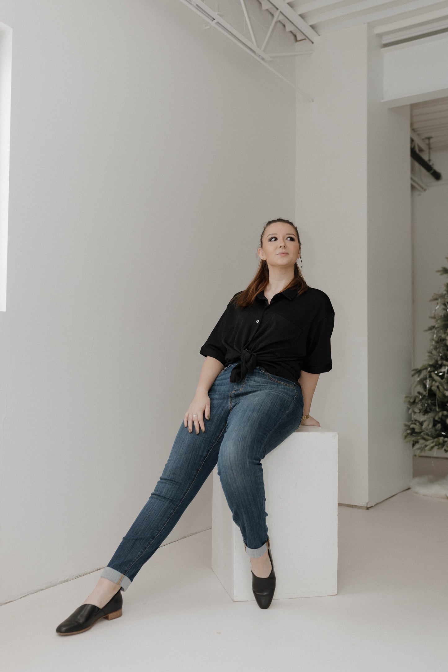 Woman sitting on a white cube in a minimalistic room with white walls and a white floor.
