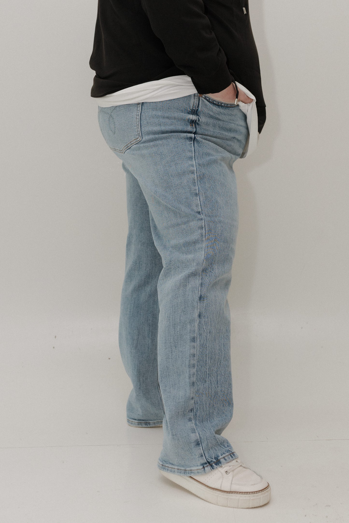 Person wearing light blue jeans and a black jacket on a white background