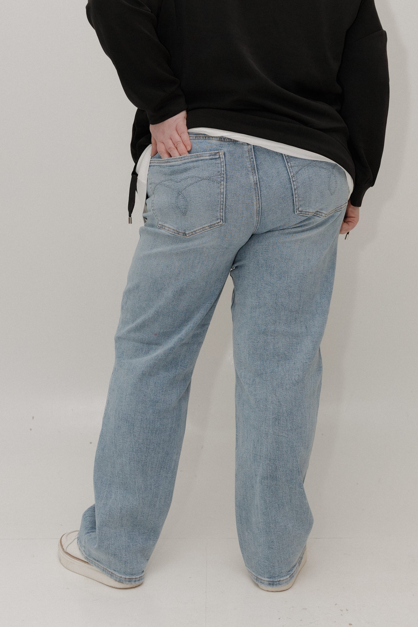 Person wearing light blue jeans and a black sweater on a white background