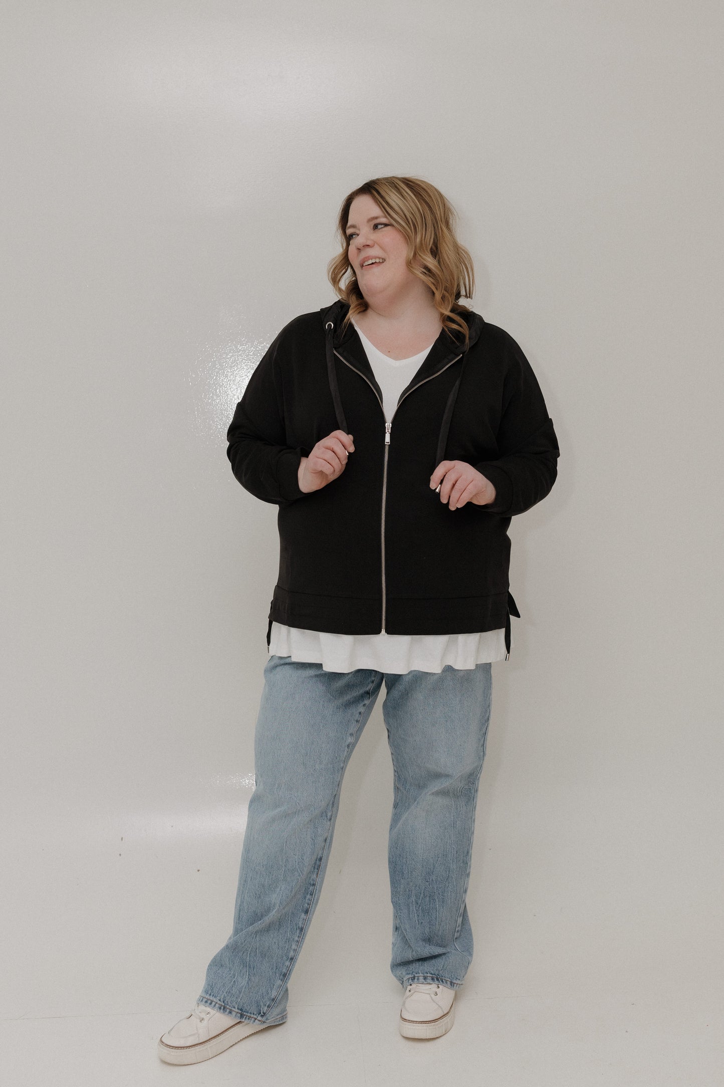 Person wearing a black jacket, white shirt, and blue jeans on a plain background