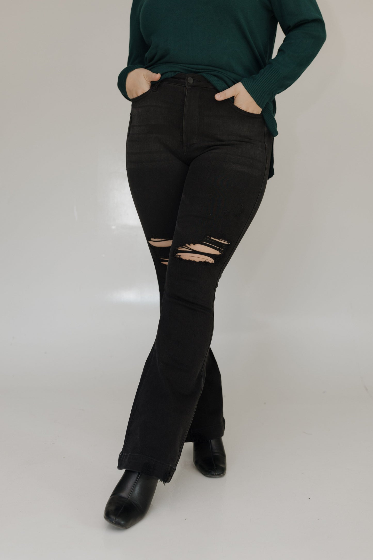 Person wearing black distressed jeans and a green top on a white background