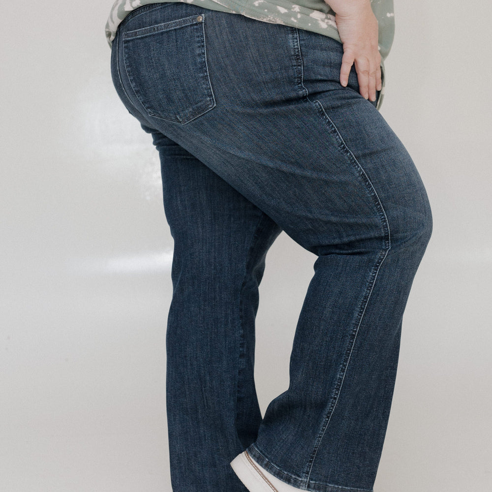 Person wearing blue jeans and a patterned shirt on a plain background