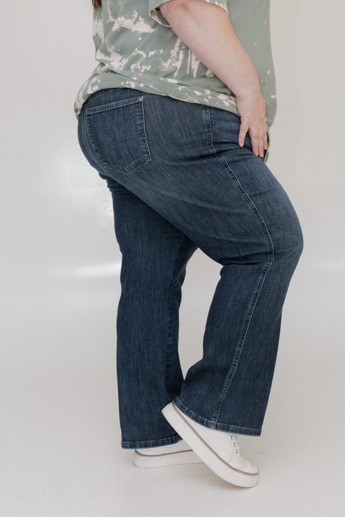 Person wearing blue jeans and a patterned shirt on a plain background
