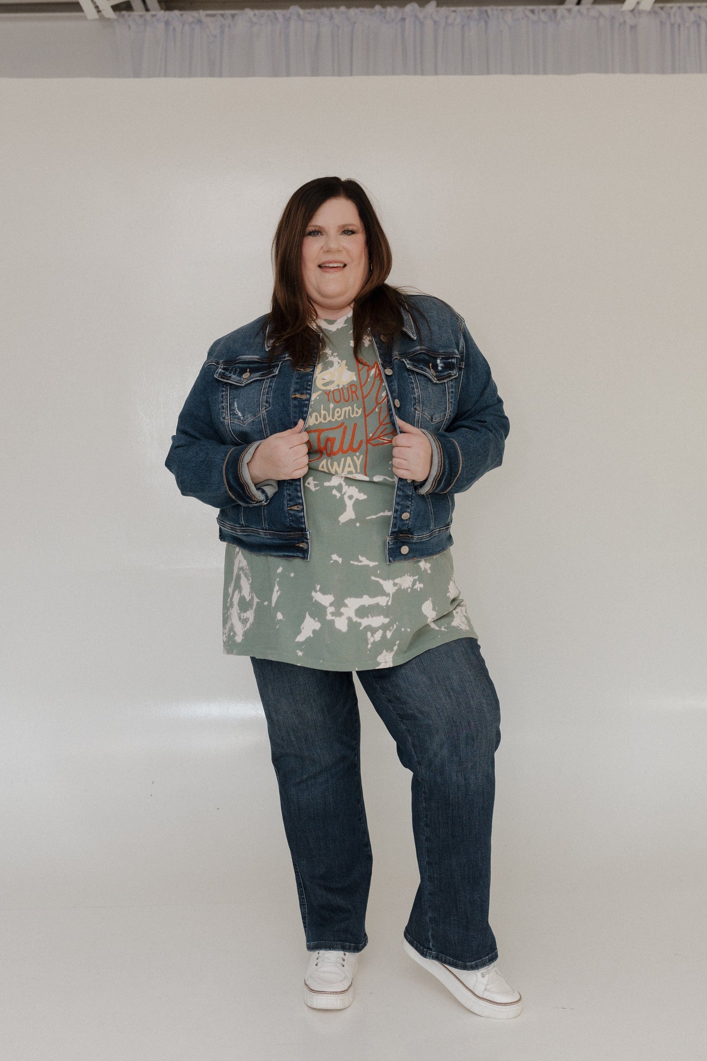 Person wearing a denim jacket, graphic t-shirt, and jeans on a plain background
