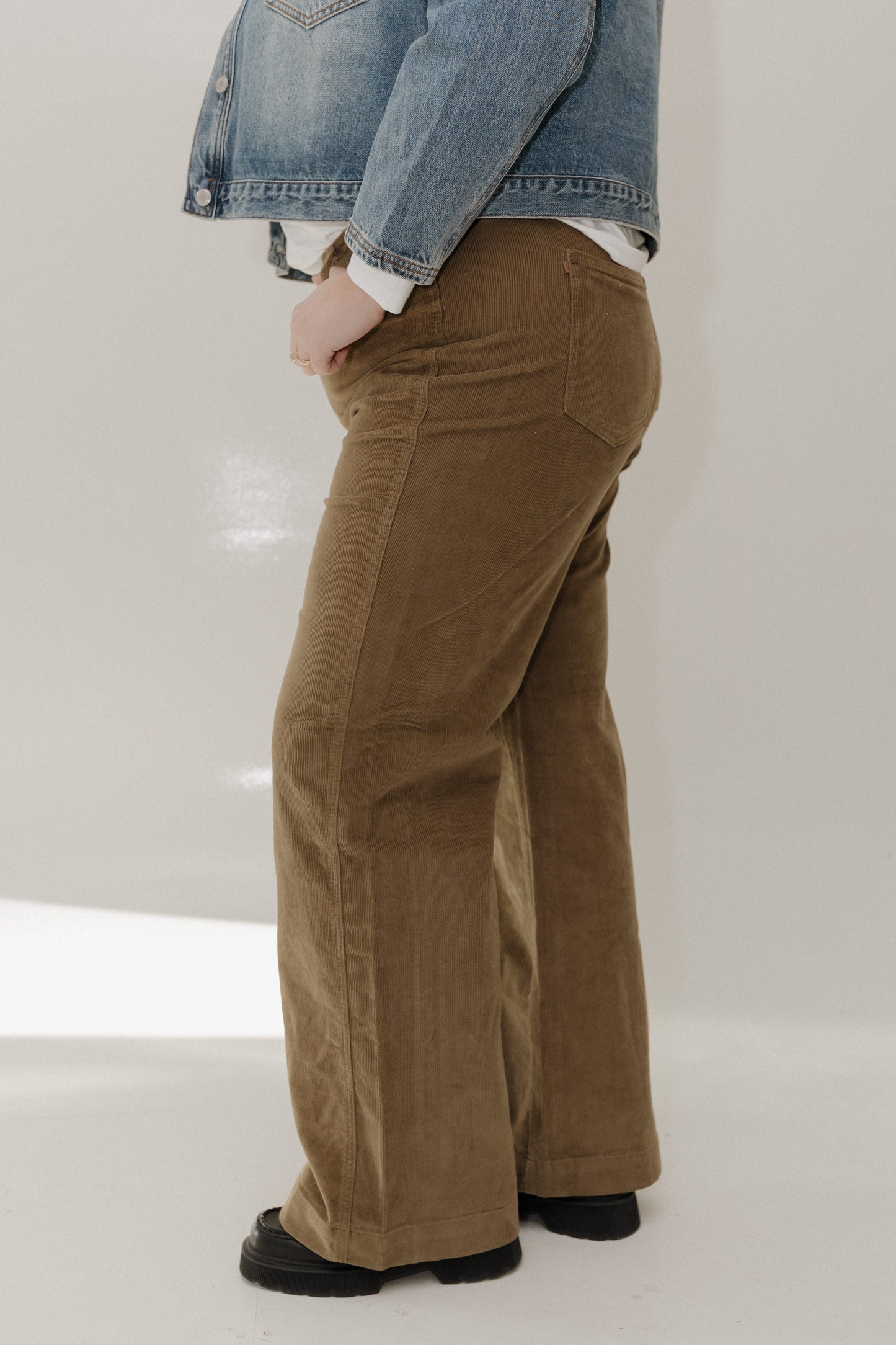 Person wearing brown corduroy pants and a denim jacket on a white background
