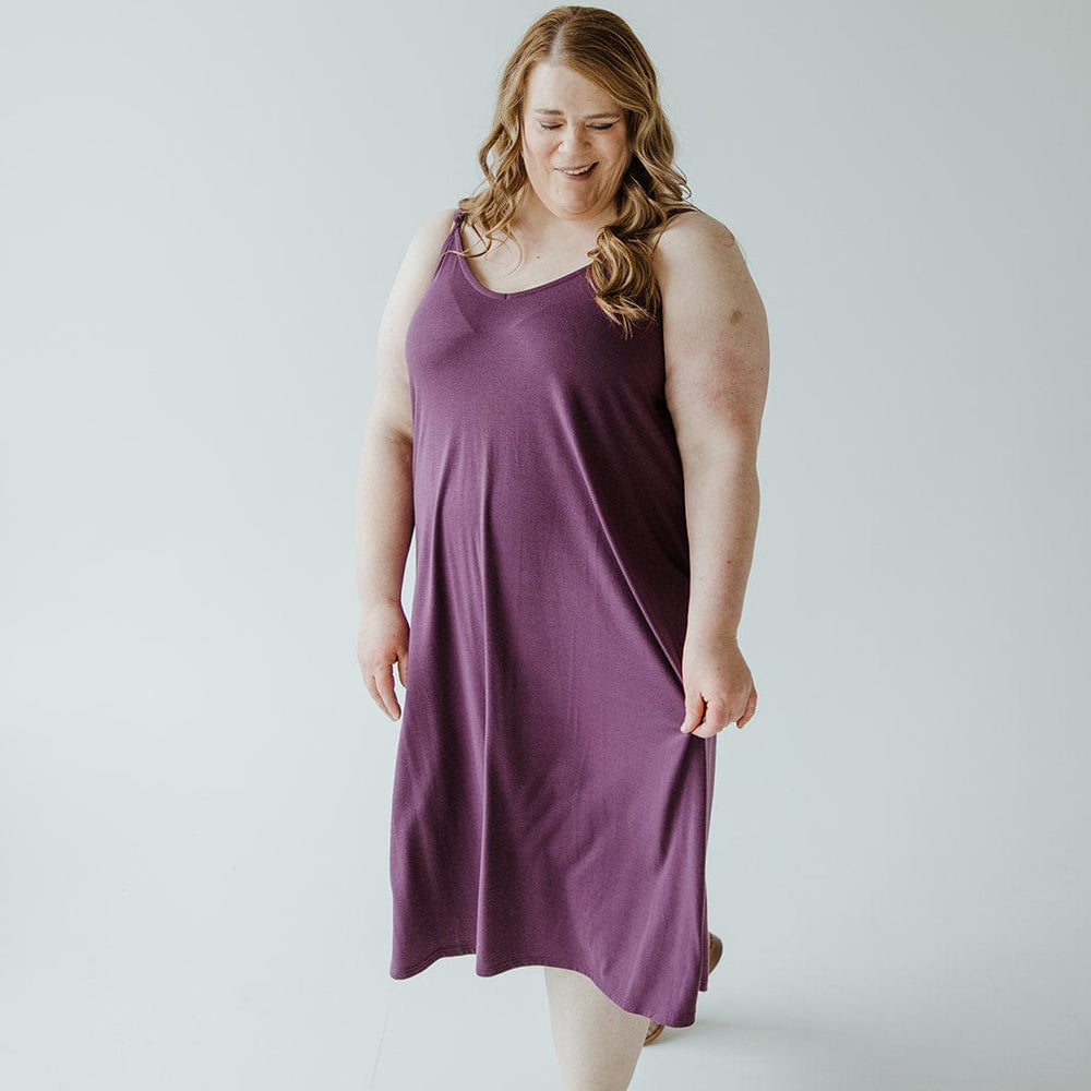 A person in an A-line cami dress of antique violet hue and brown slip-on shoes stands against a plain white background.