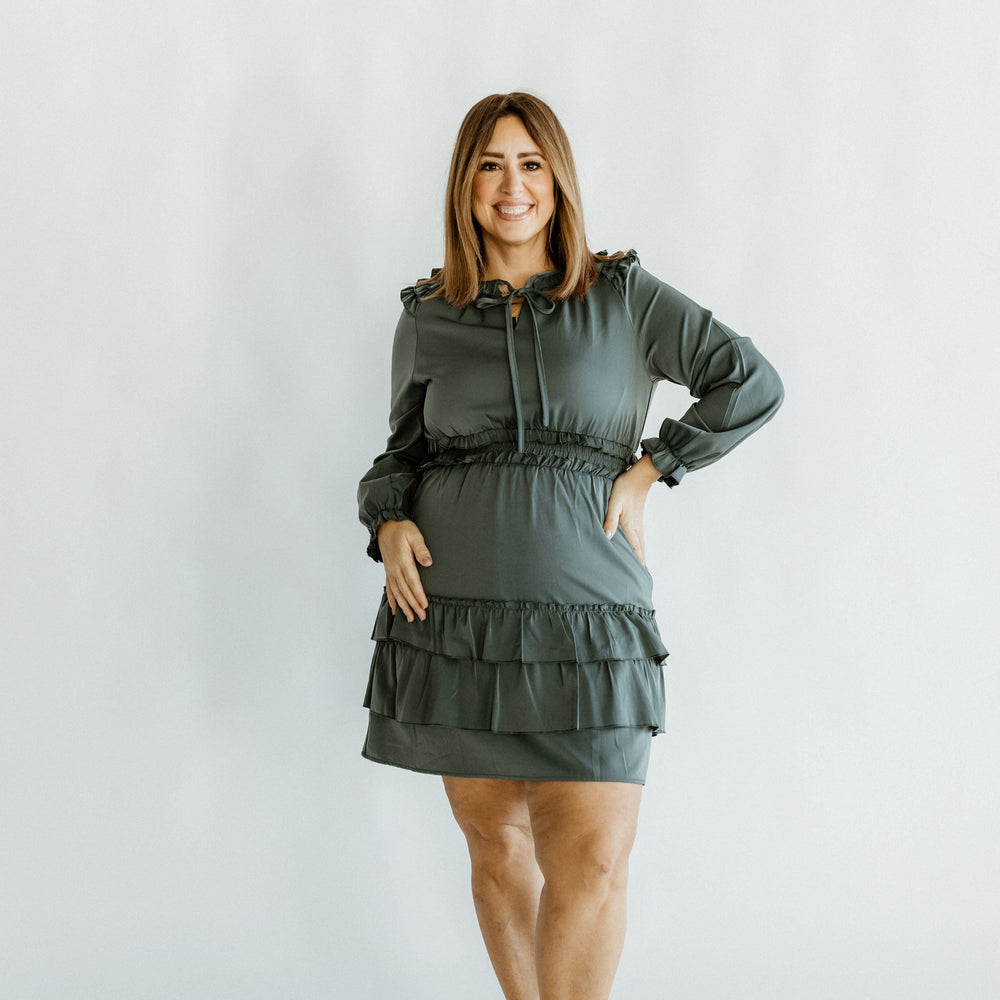 A person in a glamorous green satin dress with a tie neckline and black shoes poses elegantly against a plain background.