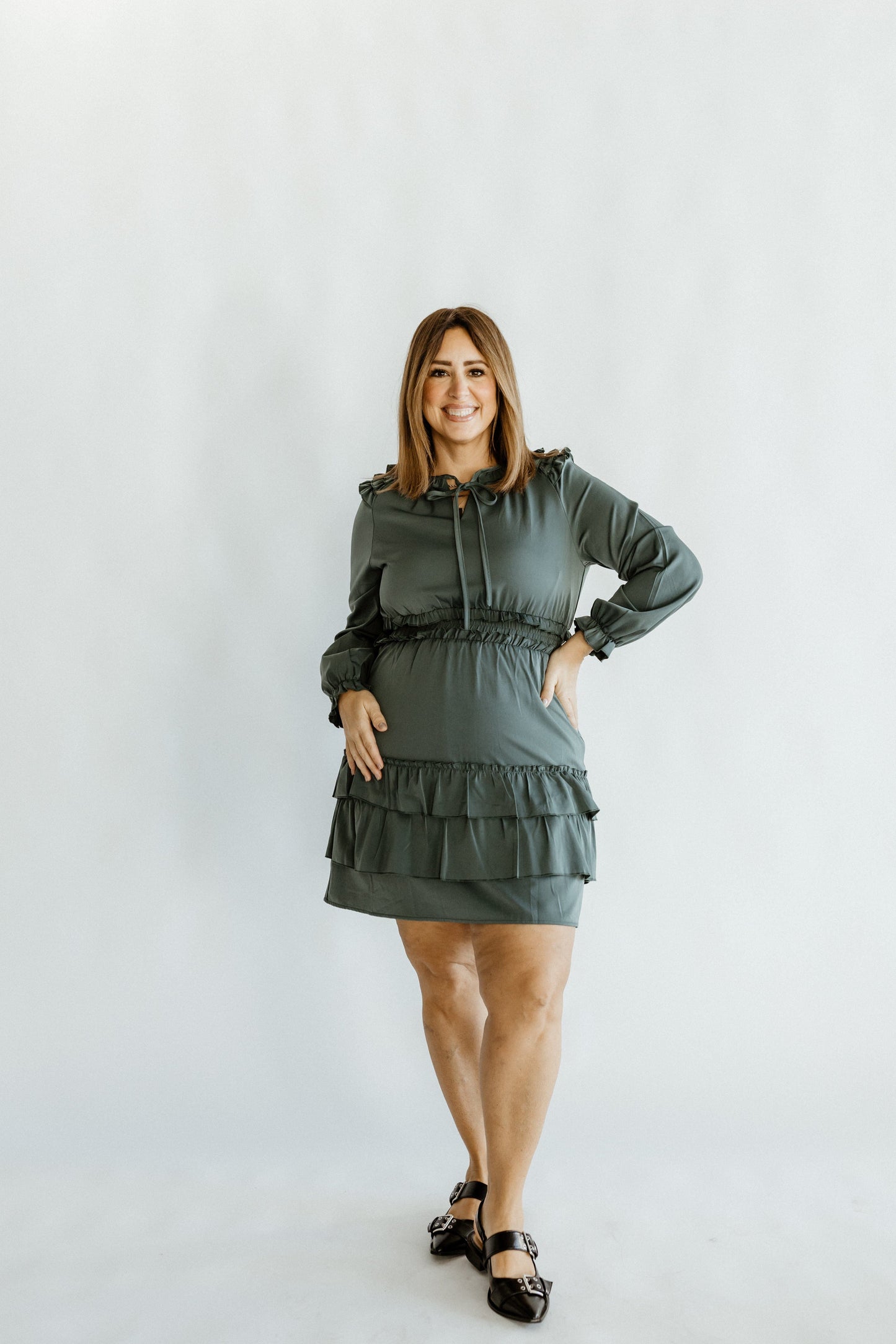 A person in a glamorous green satin dress with a tie neckline and black shoes poses elegantly against a plain background.