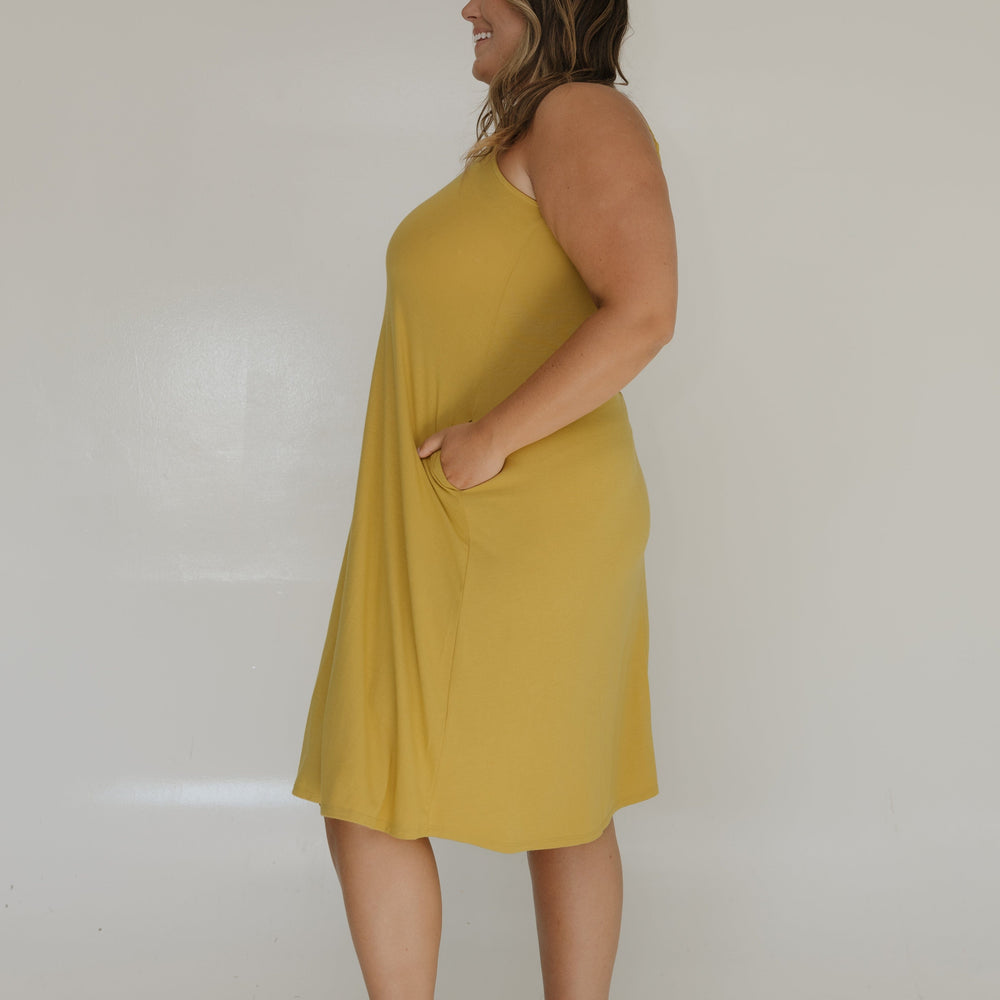 Woman wearing a yellow dress standing against a white wall.