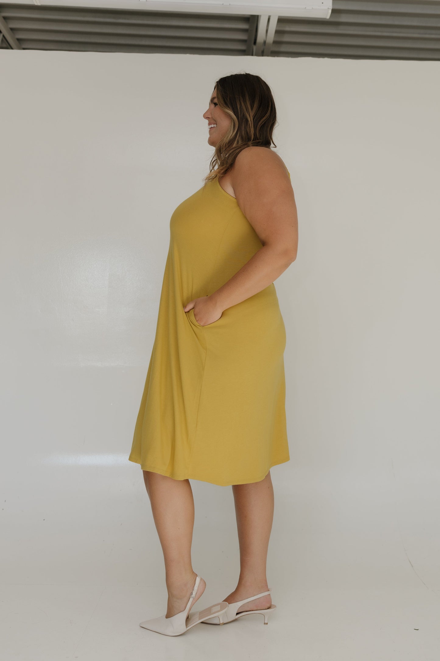 Woman wearing a yellow dress standing against a white wall.