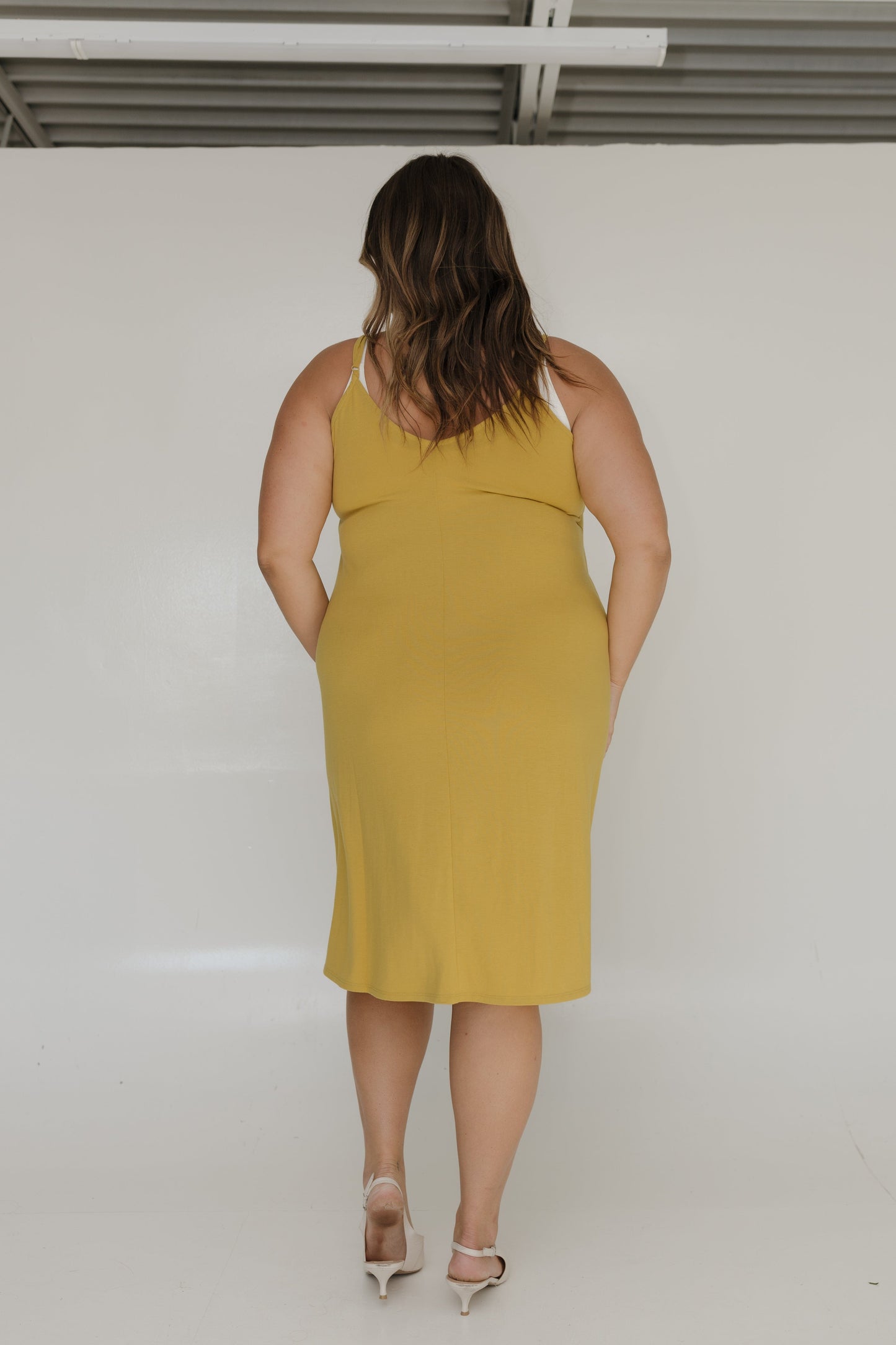 Woman wearing a yellow dress standing against a white wall.
