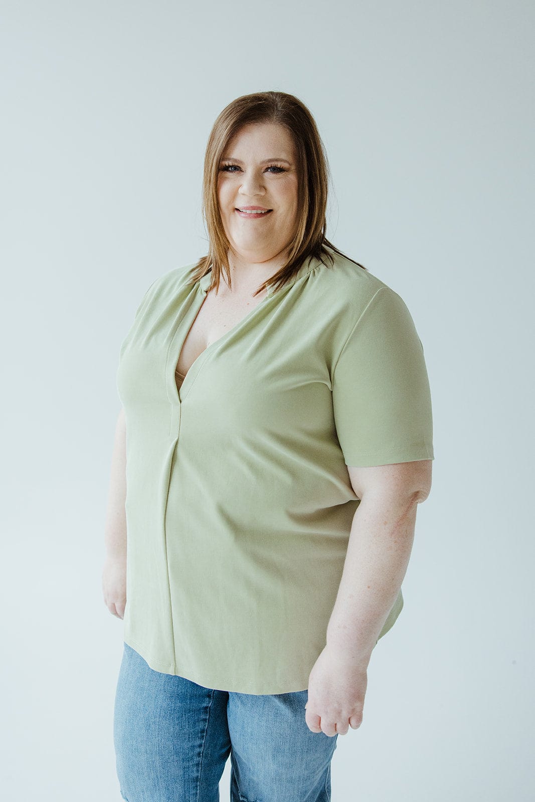 Woman with shoulder-length brown hair wearing a Love Marlow KNIT BLOUSE WITH MANDARIN COLLAR and blue jeans stands against a plain white background.