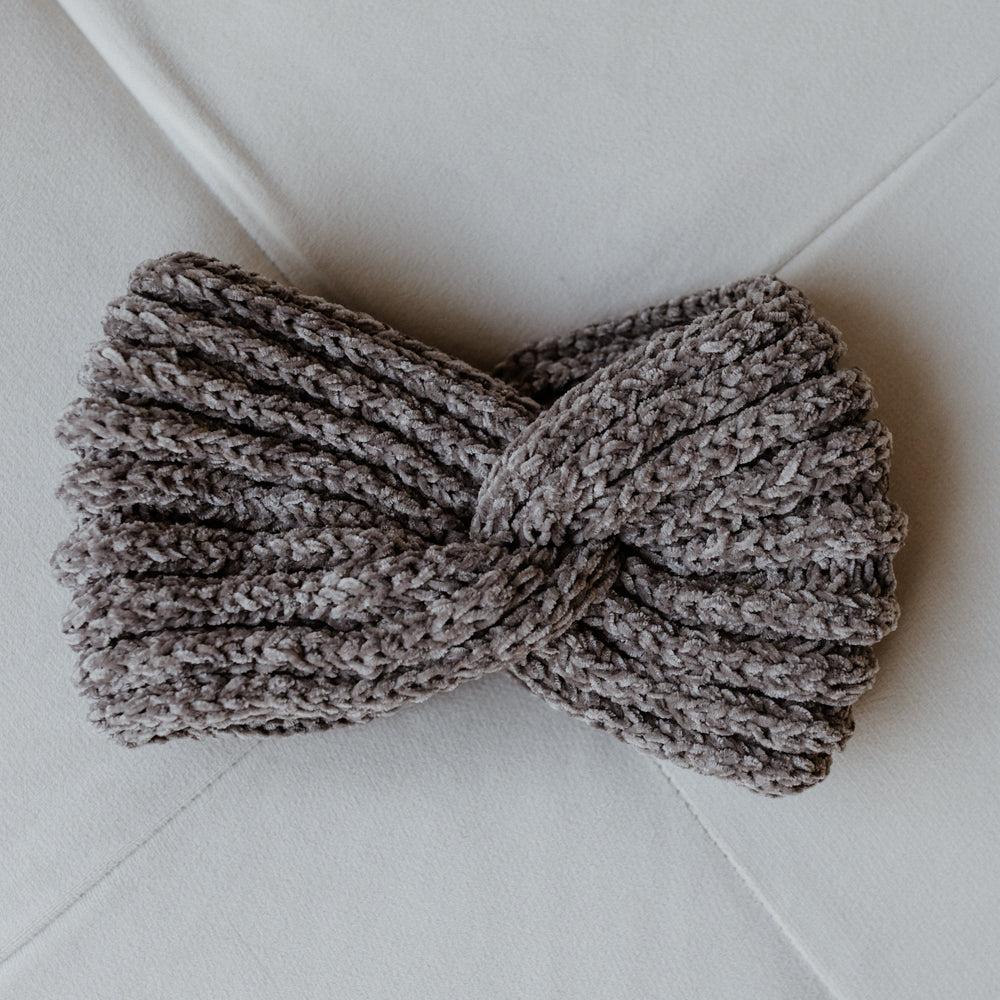 A knitted chenille headband with a twisted design rests elegantly on a white surface, perfect for adding warmth and style to any winter outfit.